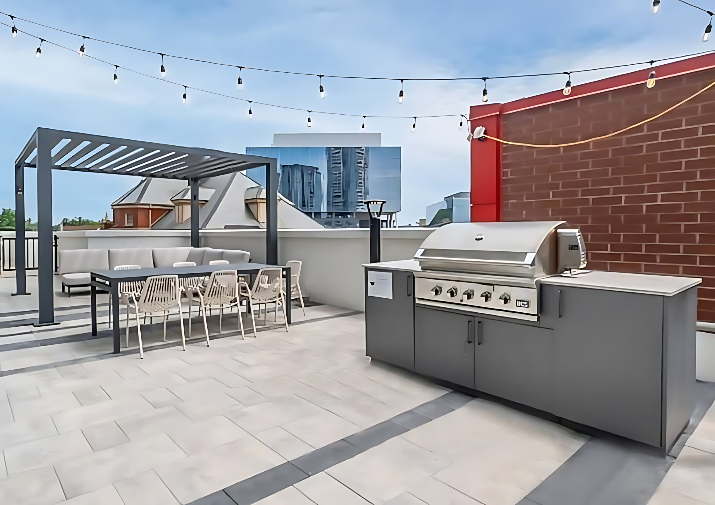 A spacious rooftop deck features an outdoor dining area with a pergola, comfortable seating, and a large built-in BBQ grill, all under string lights, offering an urban outdoor living space.