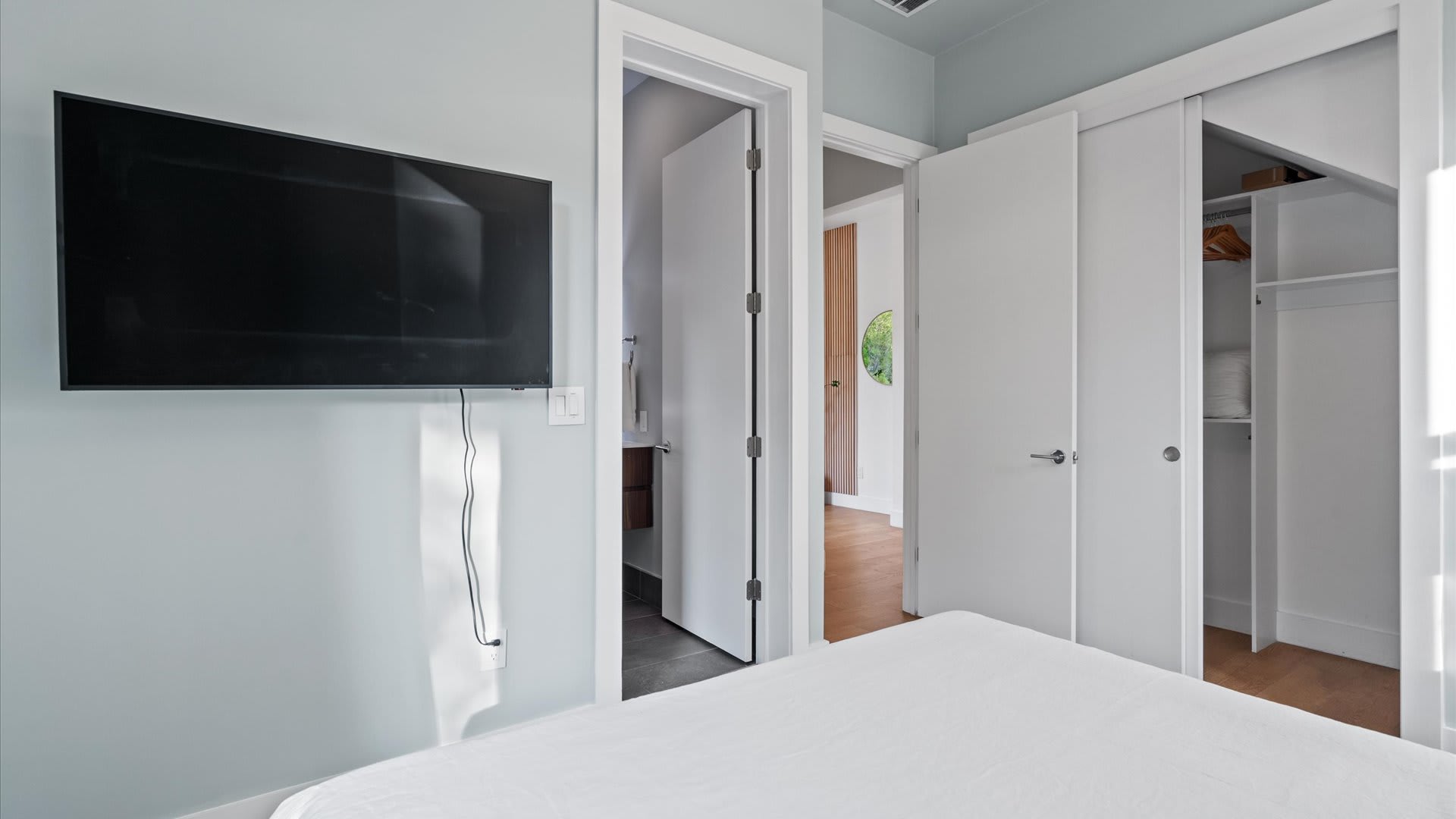 Another perspective of Bedroom-1, showcasing a wall-mounted television and a closet with white bi-fold doors. A doorway leads to an en-suite bathroom, providing convenient access.