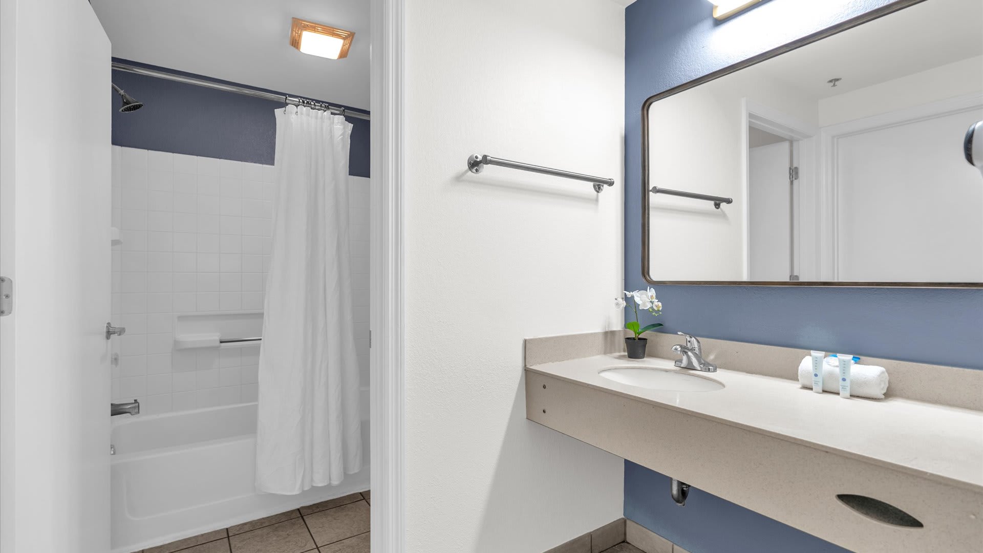 Modern bathroom with a light-colored vanity, a rectangular mirror, and a white sink. A silver towel bar is mounted on the wall, and various toiletries are neatly arranged on the counter.