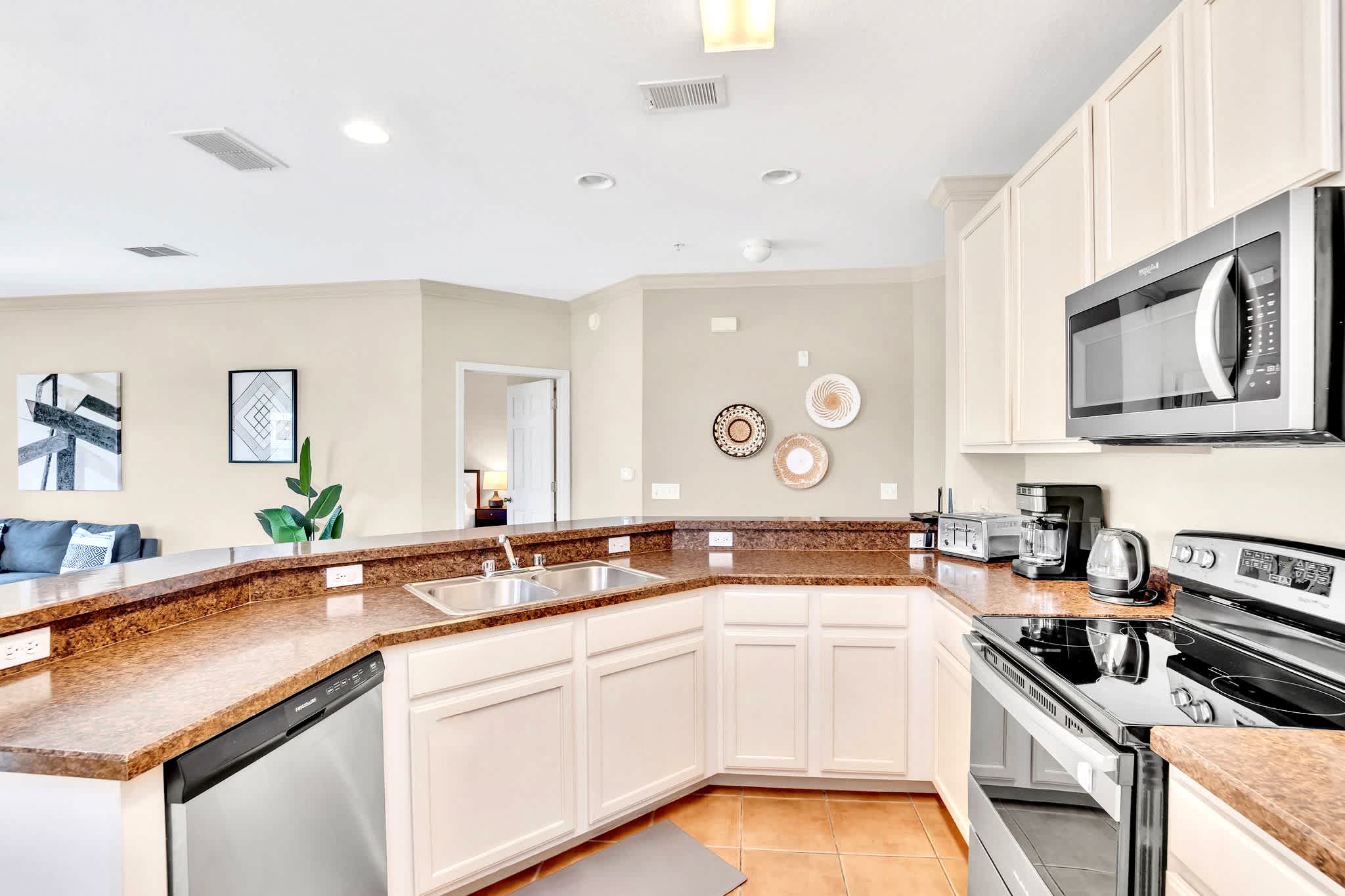U-shaped kitchen featuring white cabinets, speckled brown granite countertops, and stainless steel appliances including a double sink and dishwasher. The floor is tiled, and decorative wall plates add a touch of character.