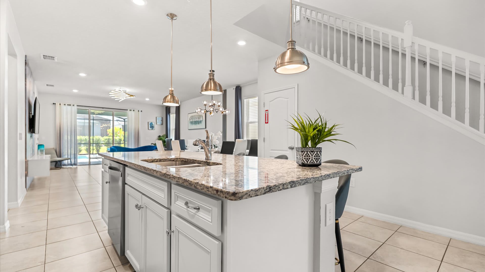 A view of the kitchen island with a sink and a potted plant, looking towards a carpeted staircase with white railings, showcasing the open layout of the ground floor.