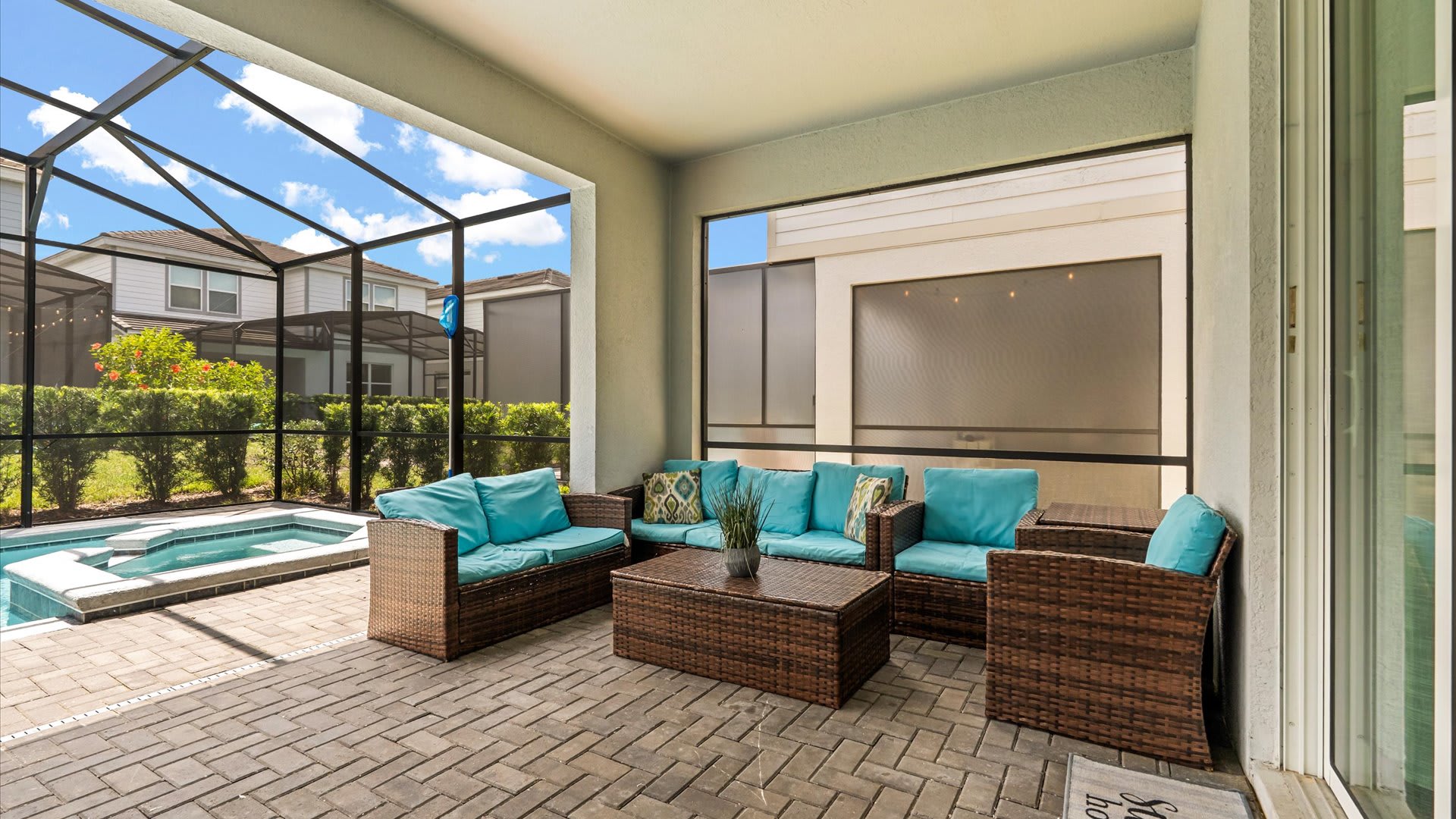 Covered outdoor patio area within a screened enclosure, furnished with comfortable wicker sofas and armchairs featuring bright blue cushions, overlooking the private pool.