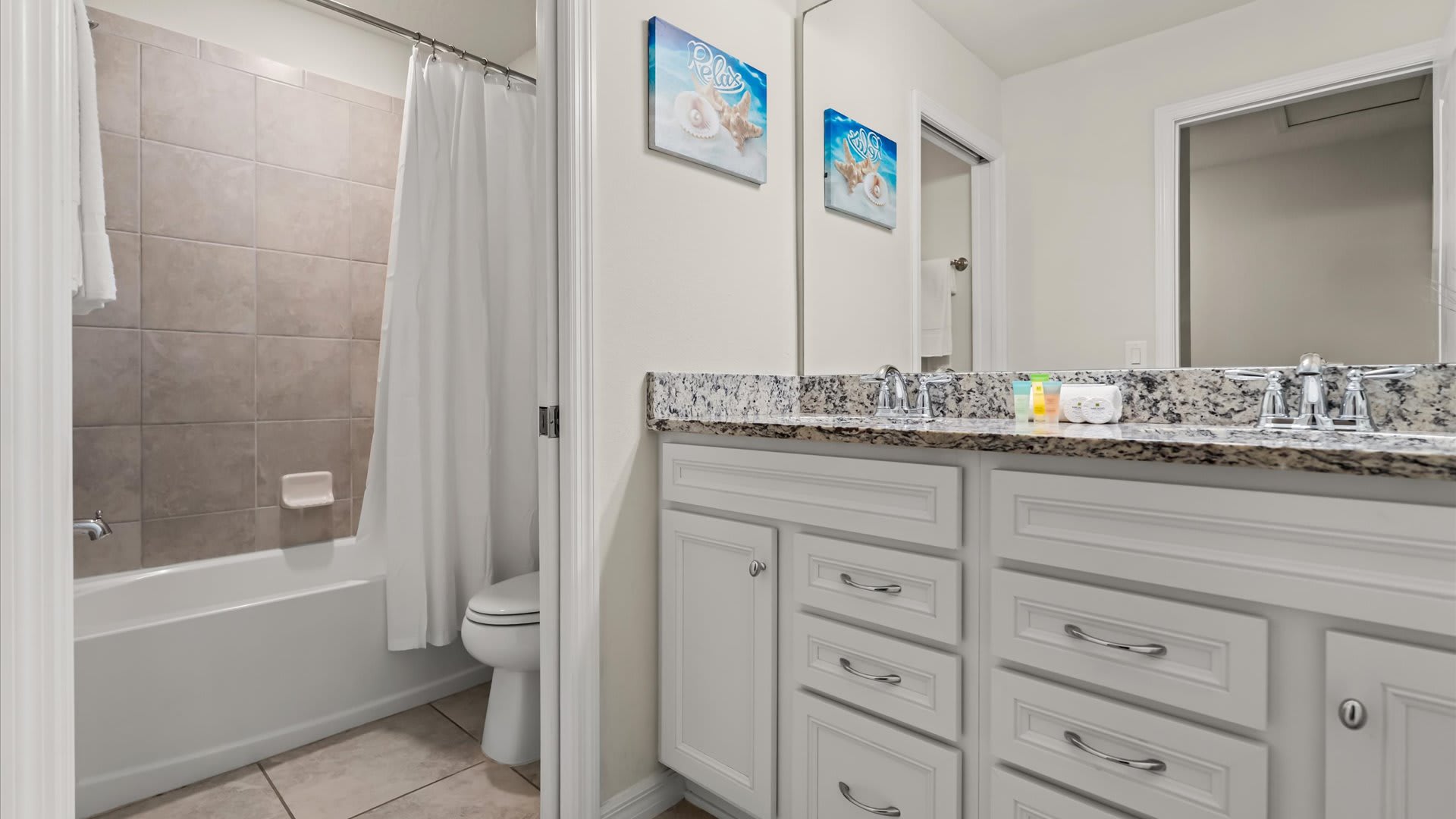 A clean, modern bathroom featuring a double vanity with granite countertops, white cabinetry, and a shower/tub combination with a white curtain and tiled walls.