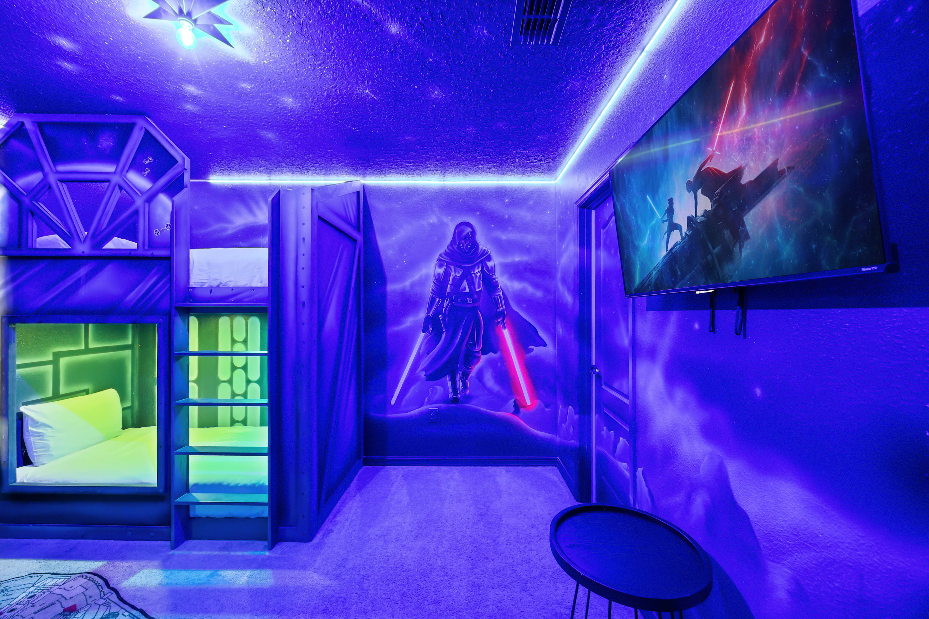 Star Wars themed bedroom illuminated with blue ambient lighting, showcasing custom bunk beds, a large Darth Vader mural, a wall-mounted TV displaying a space scene, and a small round side table.