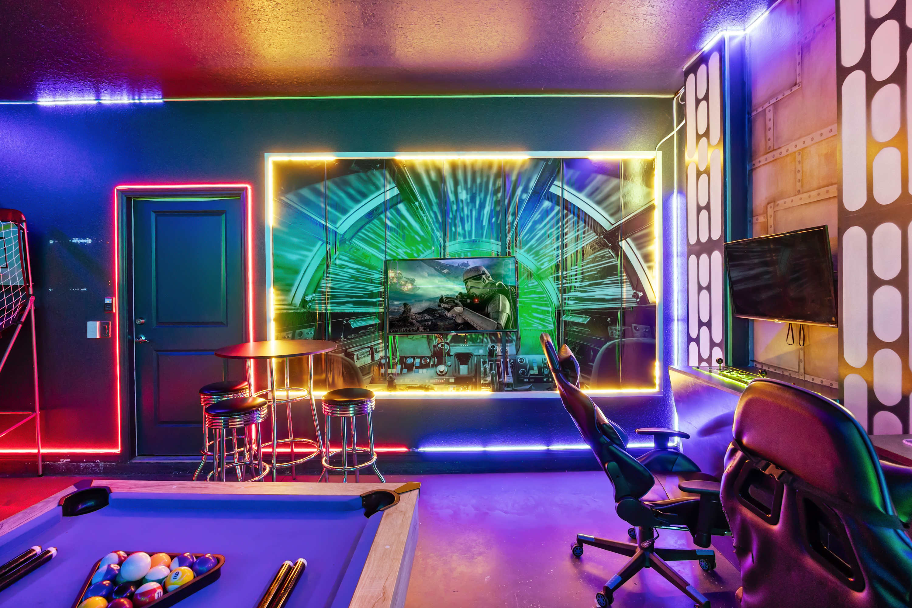 Immersive game room with a Star Wars theme, featuring a large screen displaying a game, a comfortable gaming chair, and vibrant red and yellow neon strip lighting along the walls.