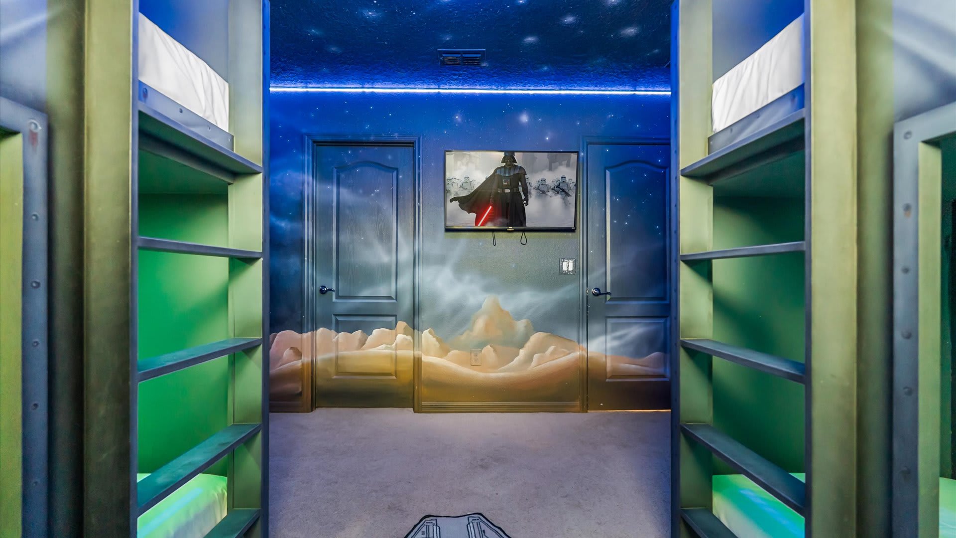 Star Wars themed bedroom with custom bunk beds flanking a central area, featuring a wall-mounted TV above two doors painted with a desert landscape mural, all under a starry ceiling.