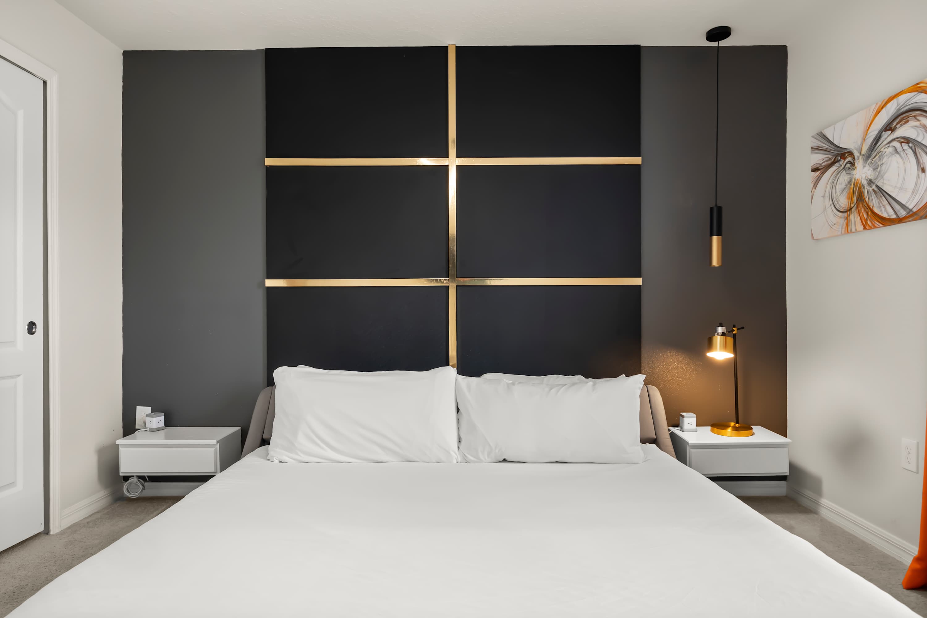 Close-up view of the stylish bedroom's grey platform bed, flanked by floating white nightstands with modern lamps, set against a black and gold accent wall.