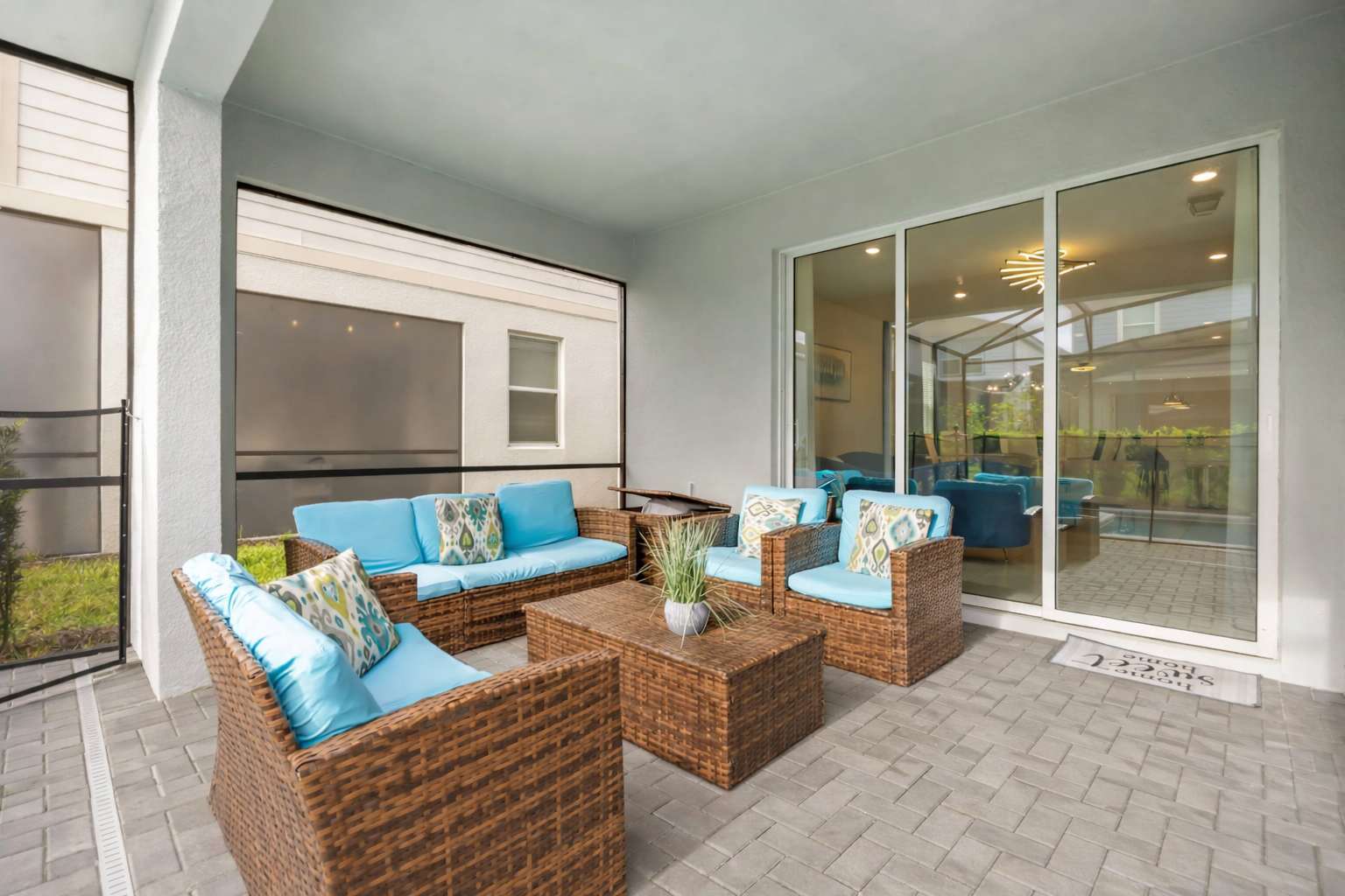 Inviting covered patio seating area furnished with a set of wicker sofas and armchairs with blue cushions, centered around a coffee table with a potted plant, adjacent to sliding glass doors.