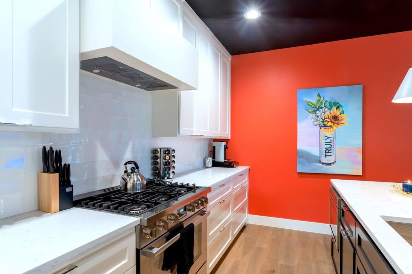 Detailed view of a modern kitchen counter with a stainless steel gas range, white subway tile backsplash, white shaker cabinets, and a kettle, set against a vibrant orange wall.