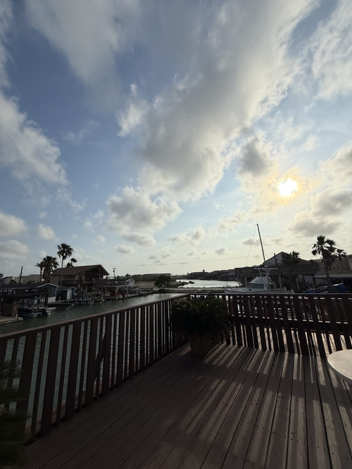 A scenic view from the deck showcasing a sunny canal filled with boats, surrounded by houses and palm trees under a bright, partly cloudy sky.