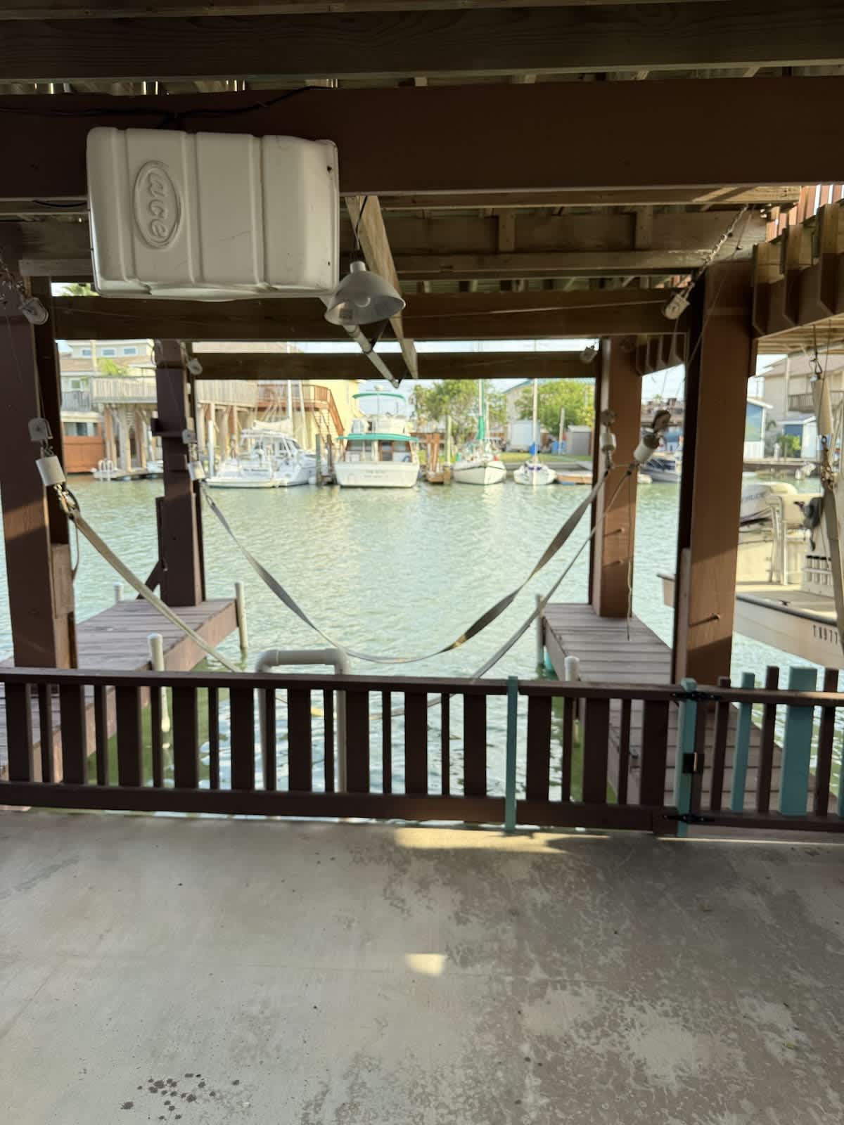 A covered boat slip area beneath the property, featuring a boat lift mechanism and a view of the canal with several boats docked nearby.