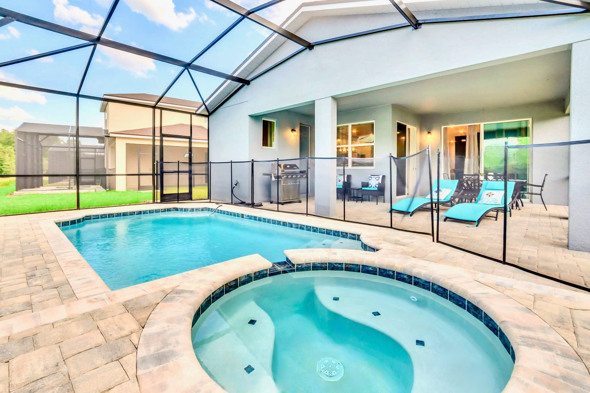 A screened-in private pool area features a rectangular swimming pool and a circular hot tub, surrounded by light-colored pavers and a safety fence, with lounge chairs and a BBQ grill visible on the patio.
