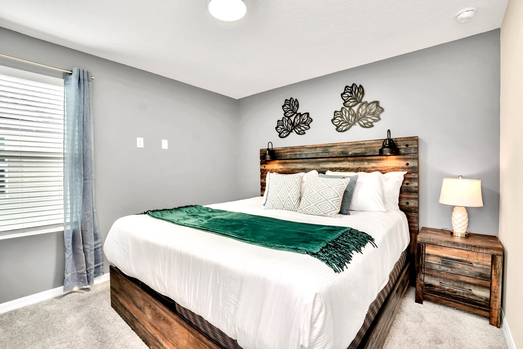 Inviting bedroom with a rustic wooden bed frame and headboard, white bedding with a green throw, two wooden nightstands with lamps, and decorative metal wall art above the bed.