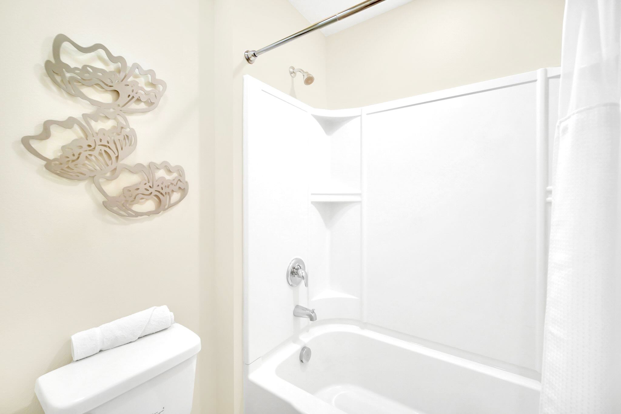 Standard bathroom with a white bathtub and shower combination, a shower curtain, and decorative wall art above the toilet.