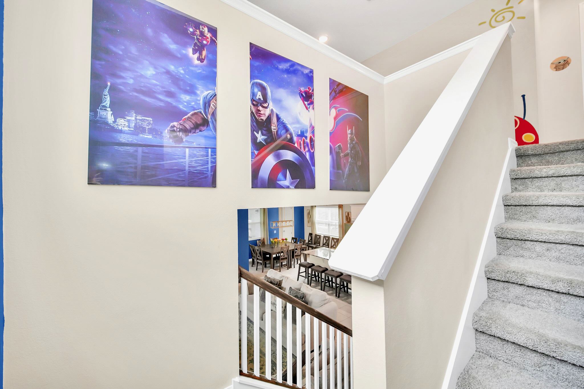 Staircase with carpeted steps and white railings, adorned with large superhero-themed canvas prints on the wall. The open-concept living and dining areas are visible below.