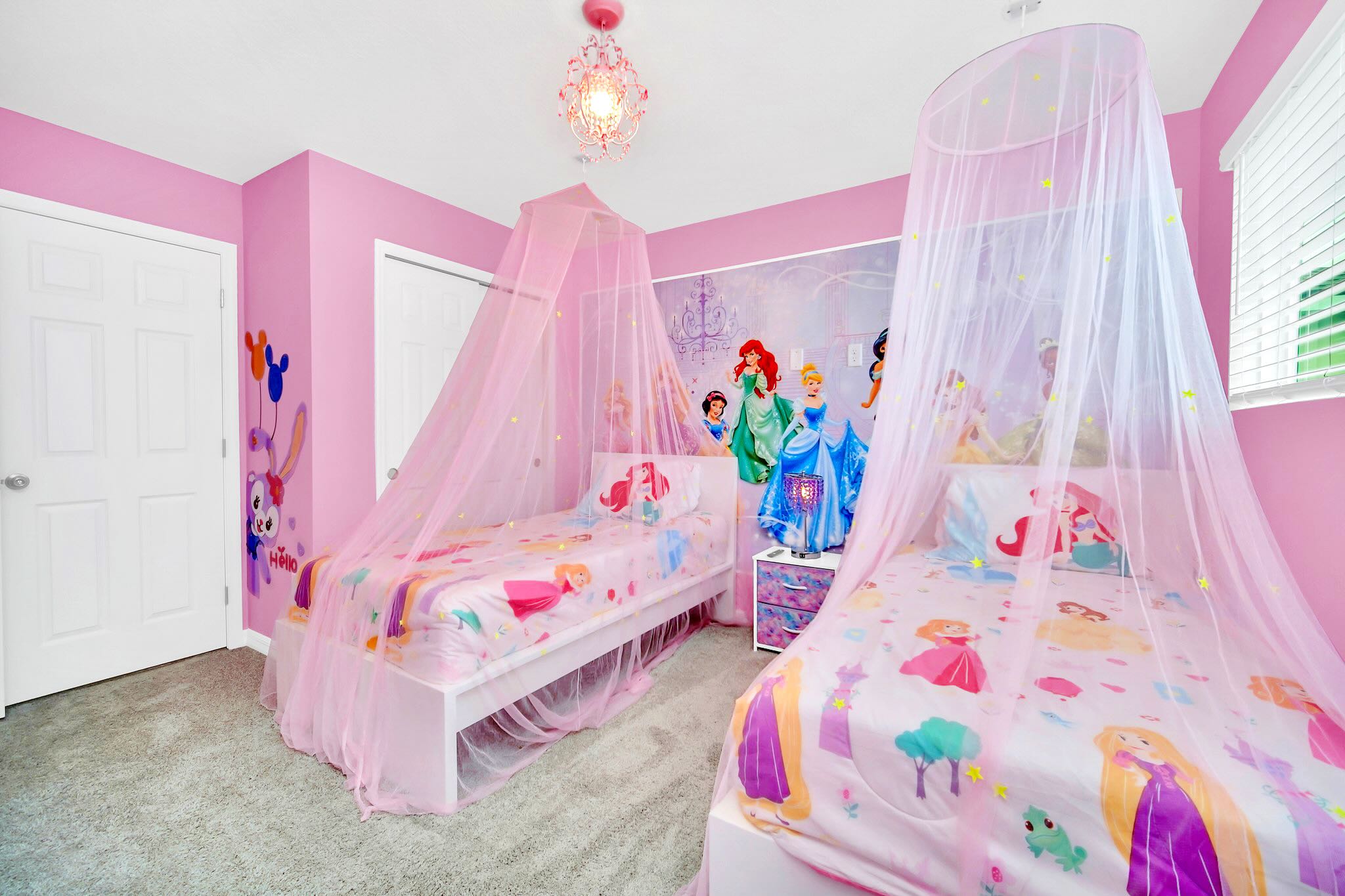 Another view of the whimsical Disney Princess themed bedroom, showcasing two twin beds with pink canopy nets, princess-themed bedding, and a colorful wall mural.