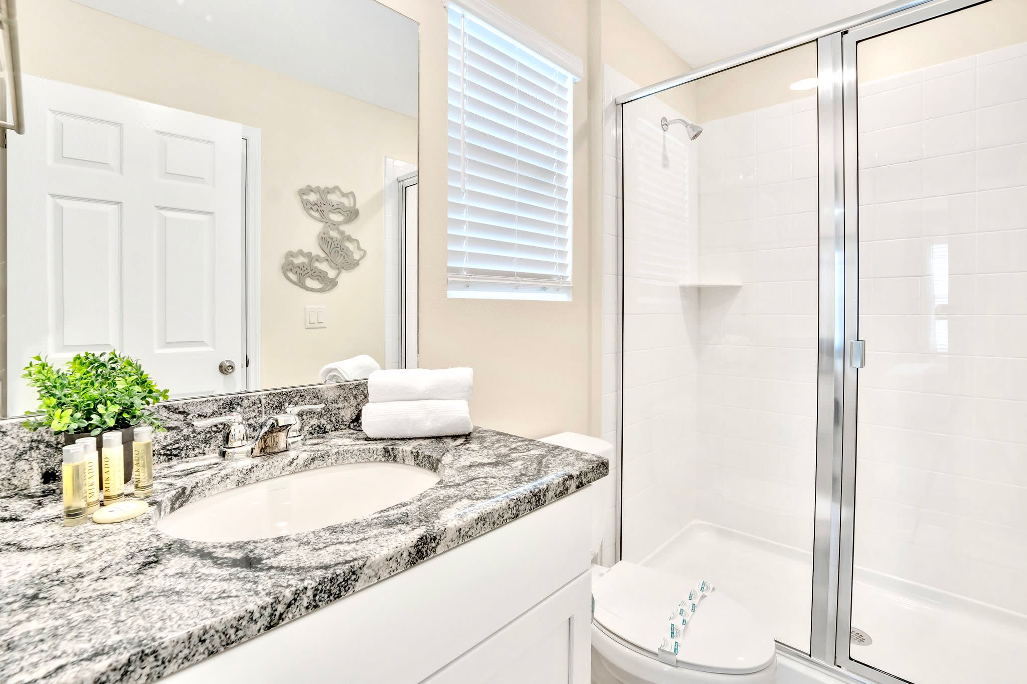 Modern bathroom featuring a single vanity with a speckled gray granite countertop, a large mirror, and a spacious walk-in shower with white subway tiles and a glass enclosure.