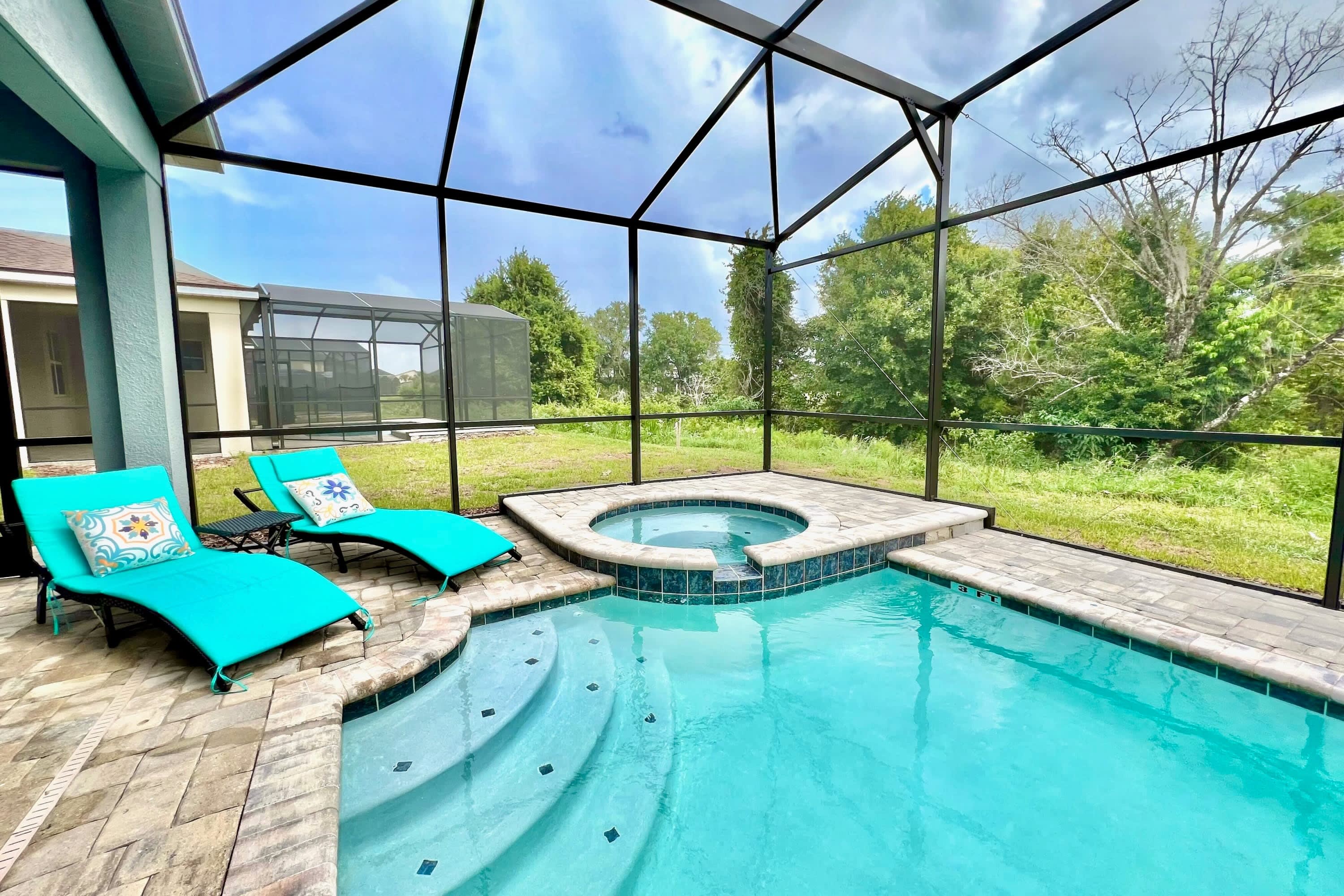 A screened-in private pool area features a rectangular swimming pool with steps and a circular hot tub, flanked by two turquoise lounge chairs on light pavers, offering a serene outdoor relaxation space.