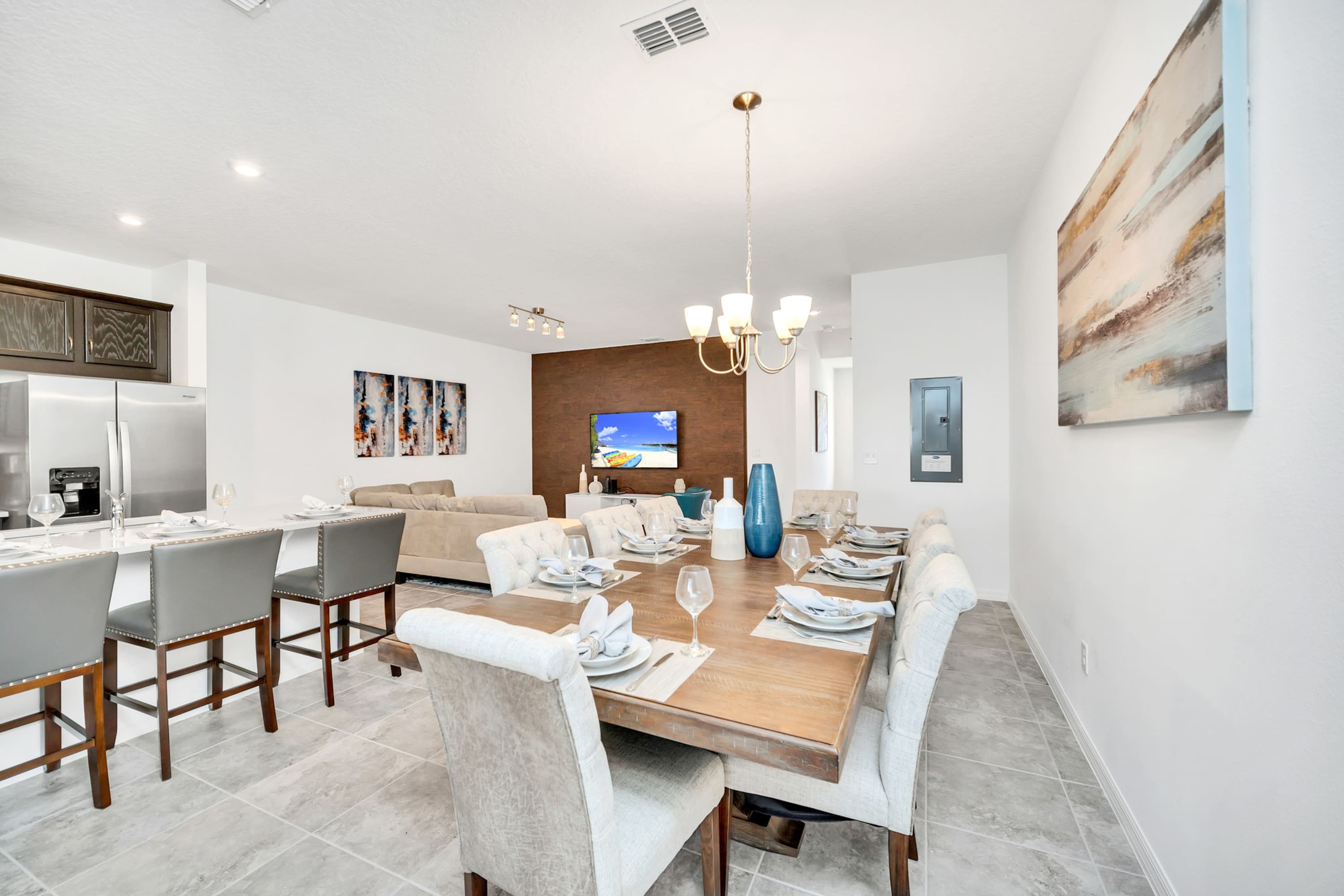 Open-concept dining area with a large wooden table and upholstered chairs, offering a clear view of the adjacent kitchen island with bar seating and the living room beyond.