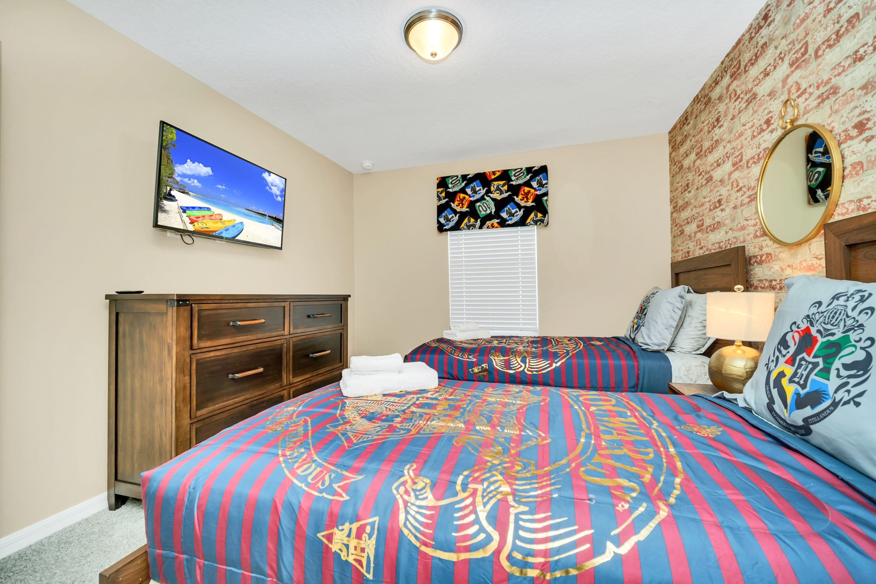 Wider view of the Harry Potter themed bedroom showing two twin beds with striped bedding, a wooden dresser with a TV, and a brick-patterned accent wall.