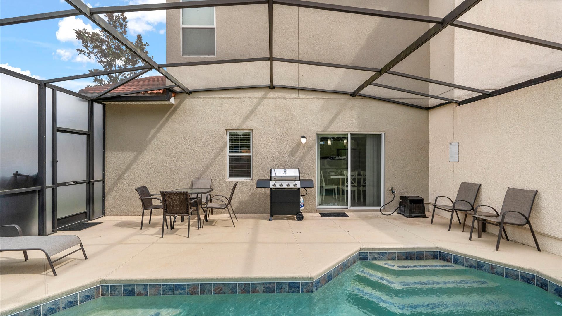 An alternative view of the screened outdoor pool area, showcasing the private pool, a BBQ grill, and various outdoor seating options on the concrete patio, enclosed by a metal frame.