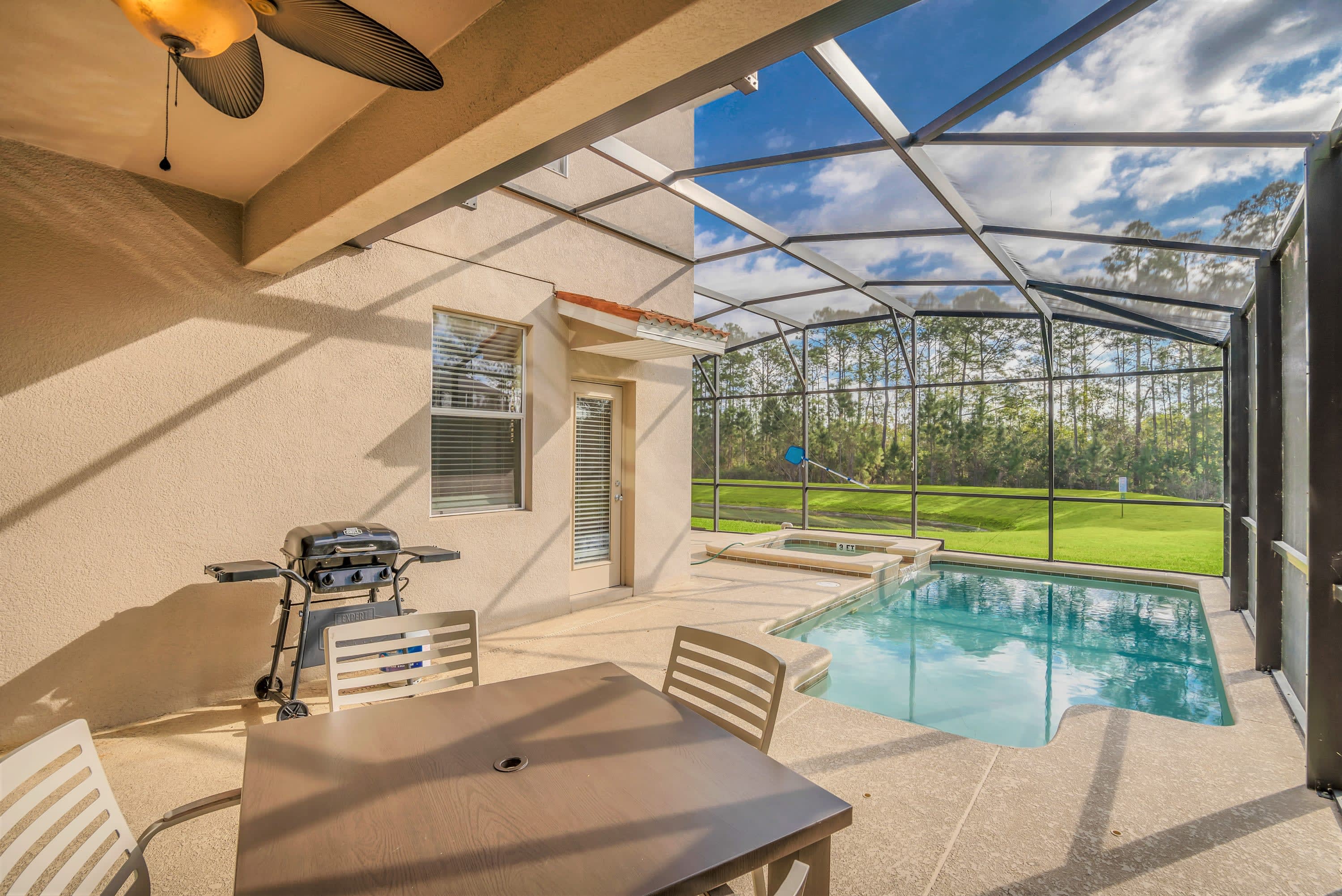 Covered outdoor patio area featuring a dining table with chairs and a BBQ grill, situated next to a screened-in private pool and hot tub.