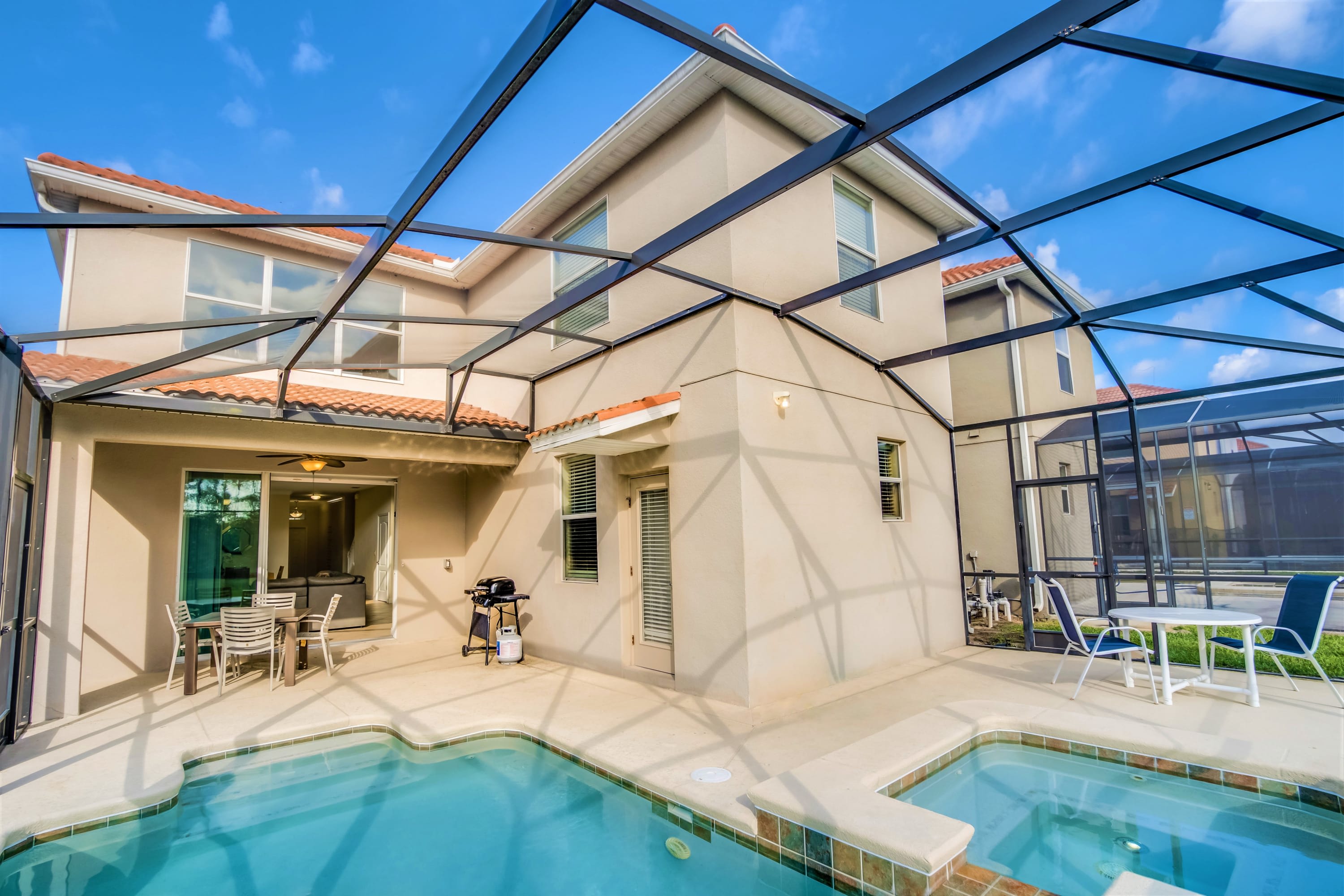 Rear view of a two-story house with a screened-in patio enclosing a private pool and hot tub, along with outdoor seating and a BBQ grill.