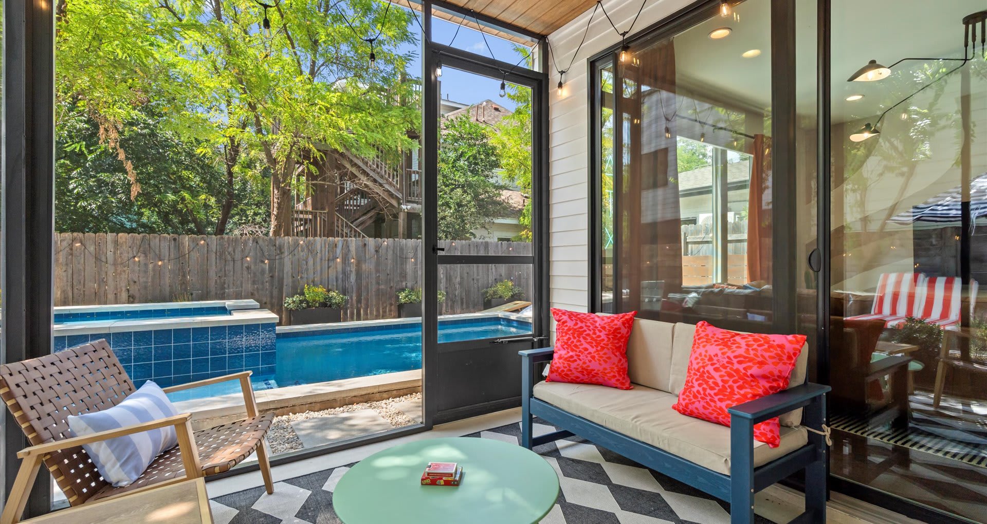 Screened-in porch with a black and white patterned rug, a light green coffee table, and comfortable seating, offering a view of the outdoor pool and backyard.