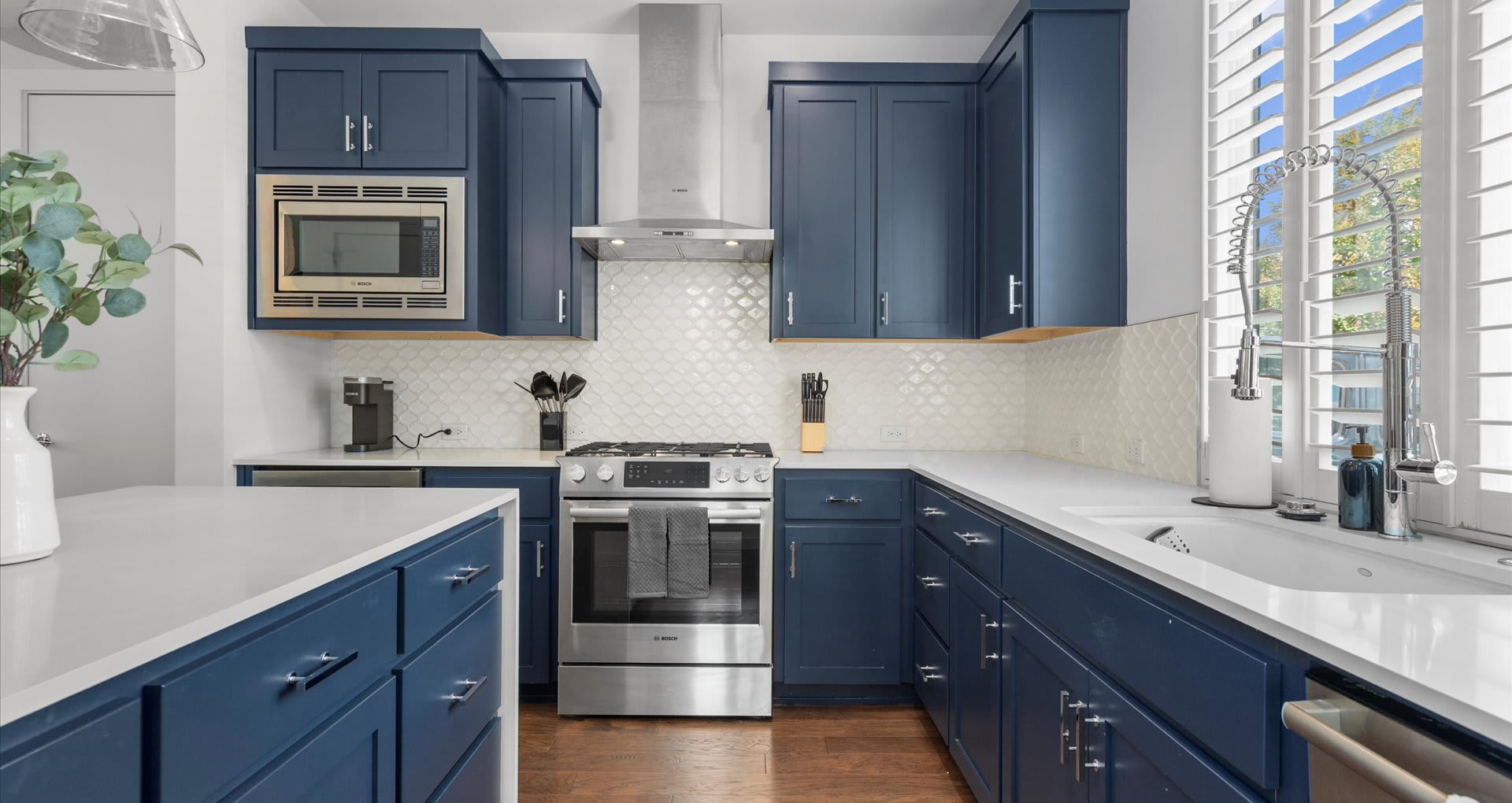 Detailed view of the kitchen's stainless steel gas range and matching hood, built-in microwave, and white scalloped tile backsplash, set against dark blue cabinetry.