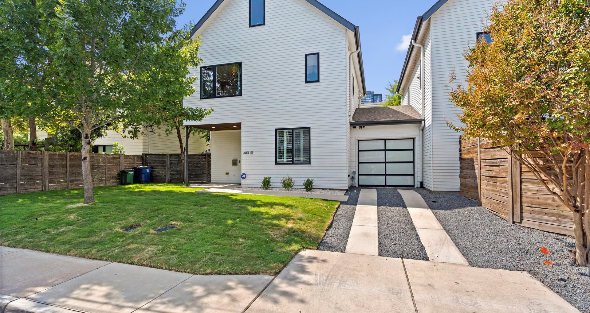 The front exterior of a modern white house with black trim windows, a dark gray garage door, and a small front yard with green grass and a gravel driveway.