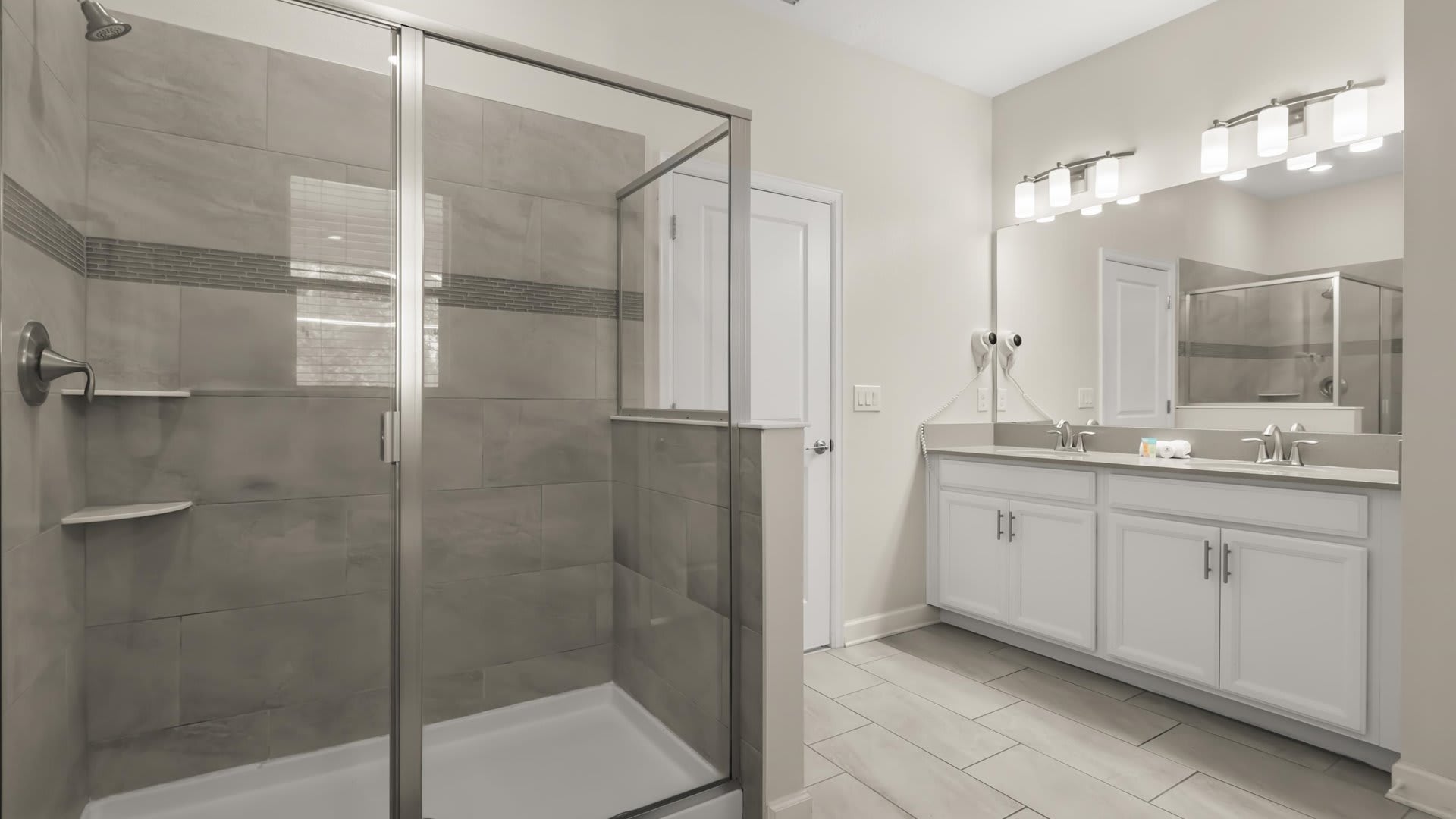Modern walk-in shower with a glass enclosure and gray subway tile walls, featuring a decorative accent strip. The shower is adjacent to the double vanity area, maintaining a clean and contemporary aesthetic.