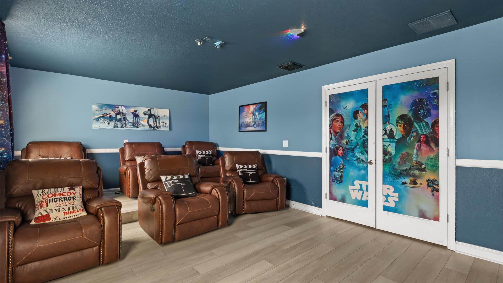 A dedicated home cinema room with dark blue walls and ceiling, featuring multiple rows of brown leather reclining chairs, Star Wars themed decor, and a subtle projector light effect on the ceiling.