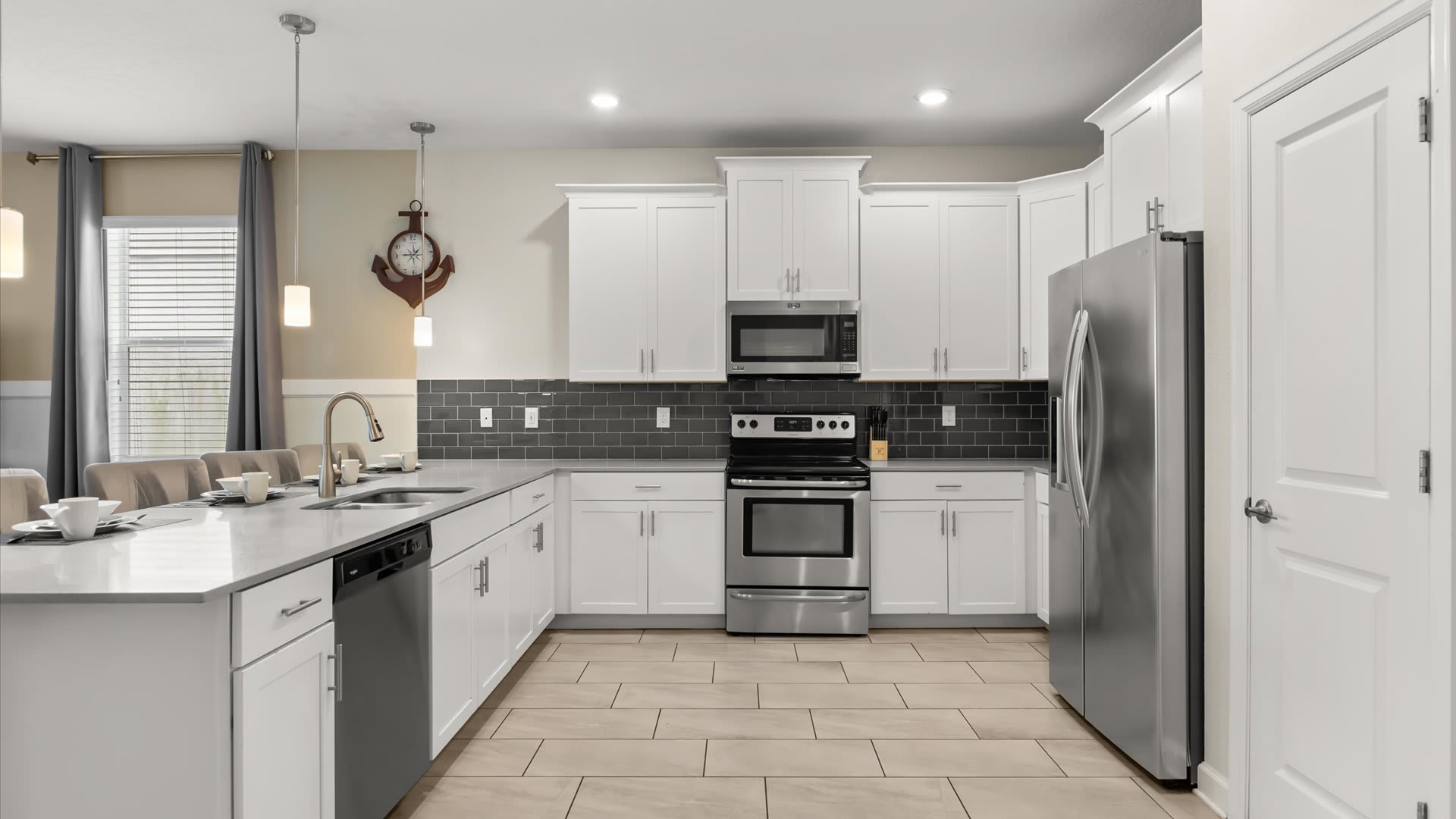 Spacious and bright kitchen with white shaker cabinets, stainless steel appliances including a refrigerator, oven, and microwave, and a dark grey subway tile backsplash, with ample counter space.