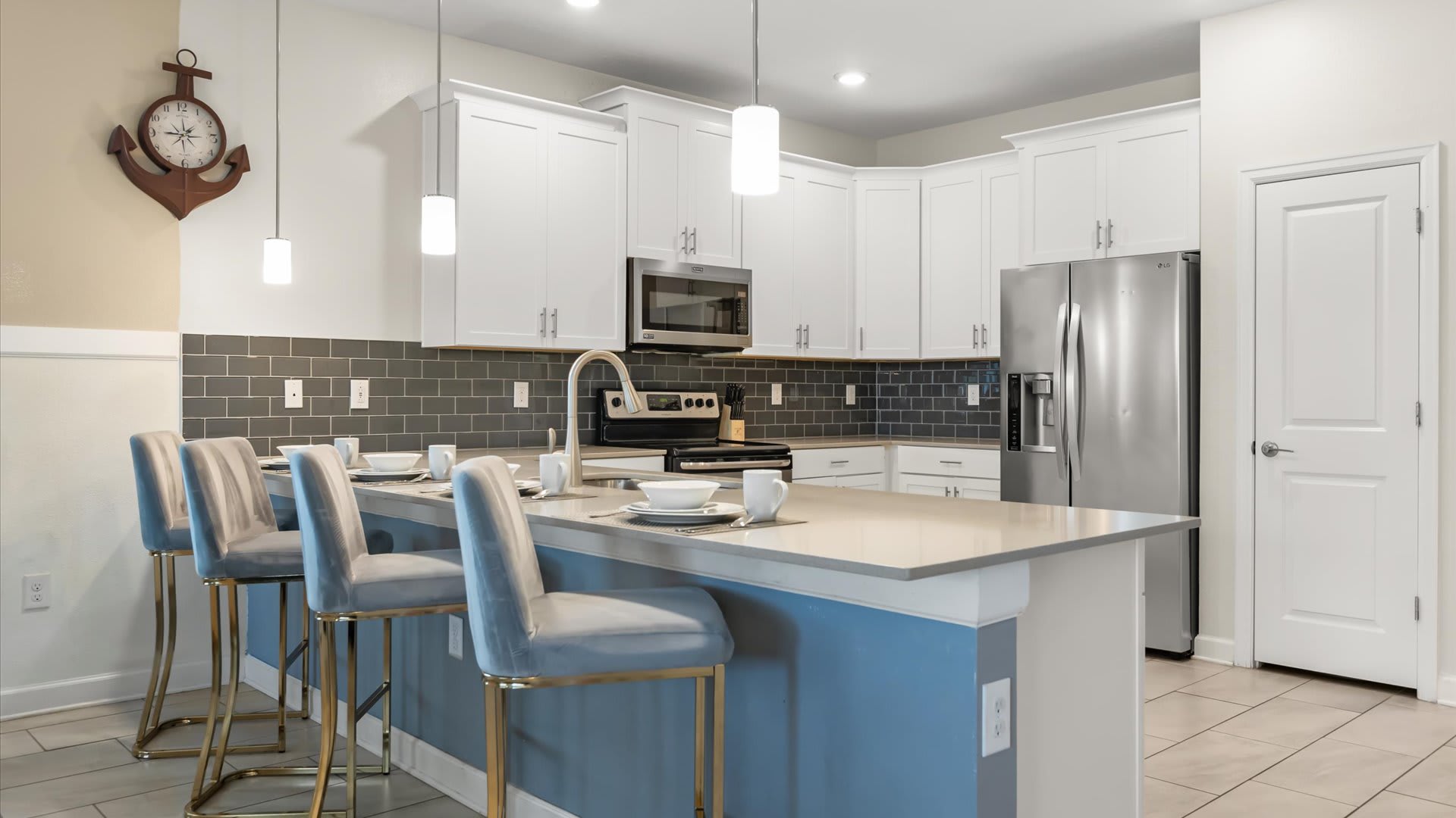 Contemporary kitchen island with a light countertop and blue base, featuring four grey velvet bar stools with gold accents, and pendant lighting, ready for casual dining.