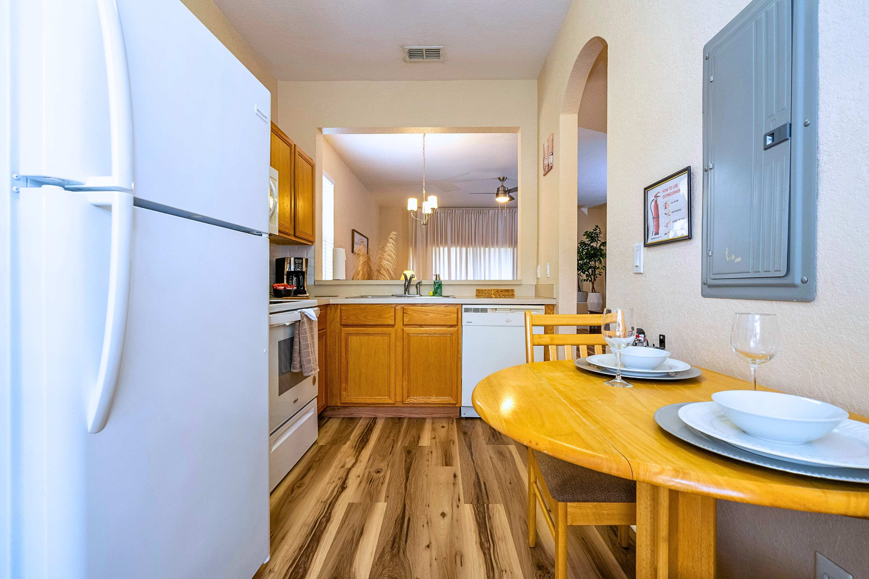 Corner view of the kitchen showing a white dishwasher, sink area, and a small round wooden breakfast table with two chairs, with a pass-through window looking into another room.