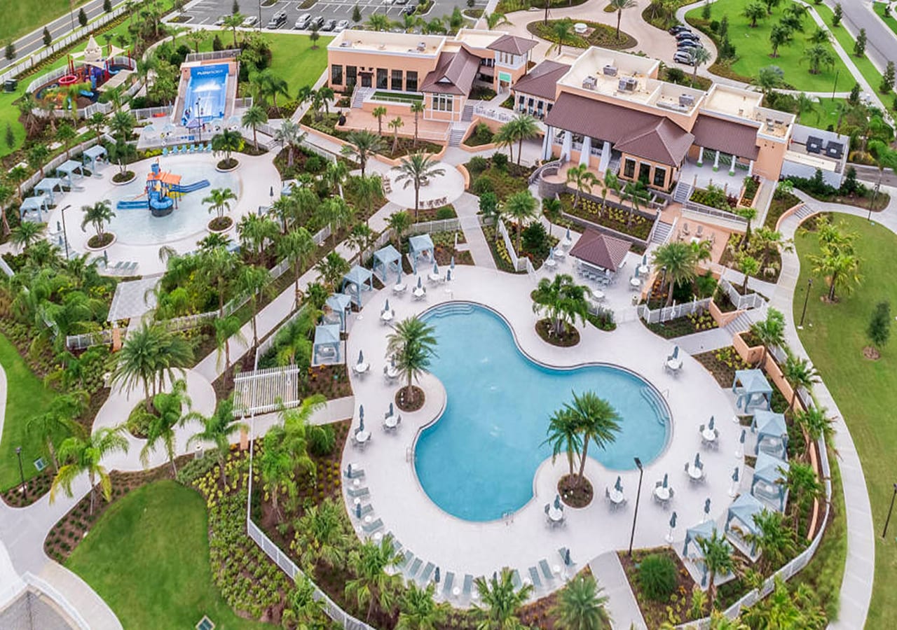 Aerial view of a large community amenity center featuring multiple swimming pools, water slides, cabanas, lounge areas, and lush landscaping with palm trees.