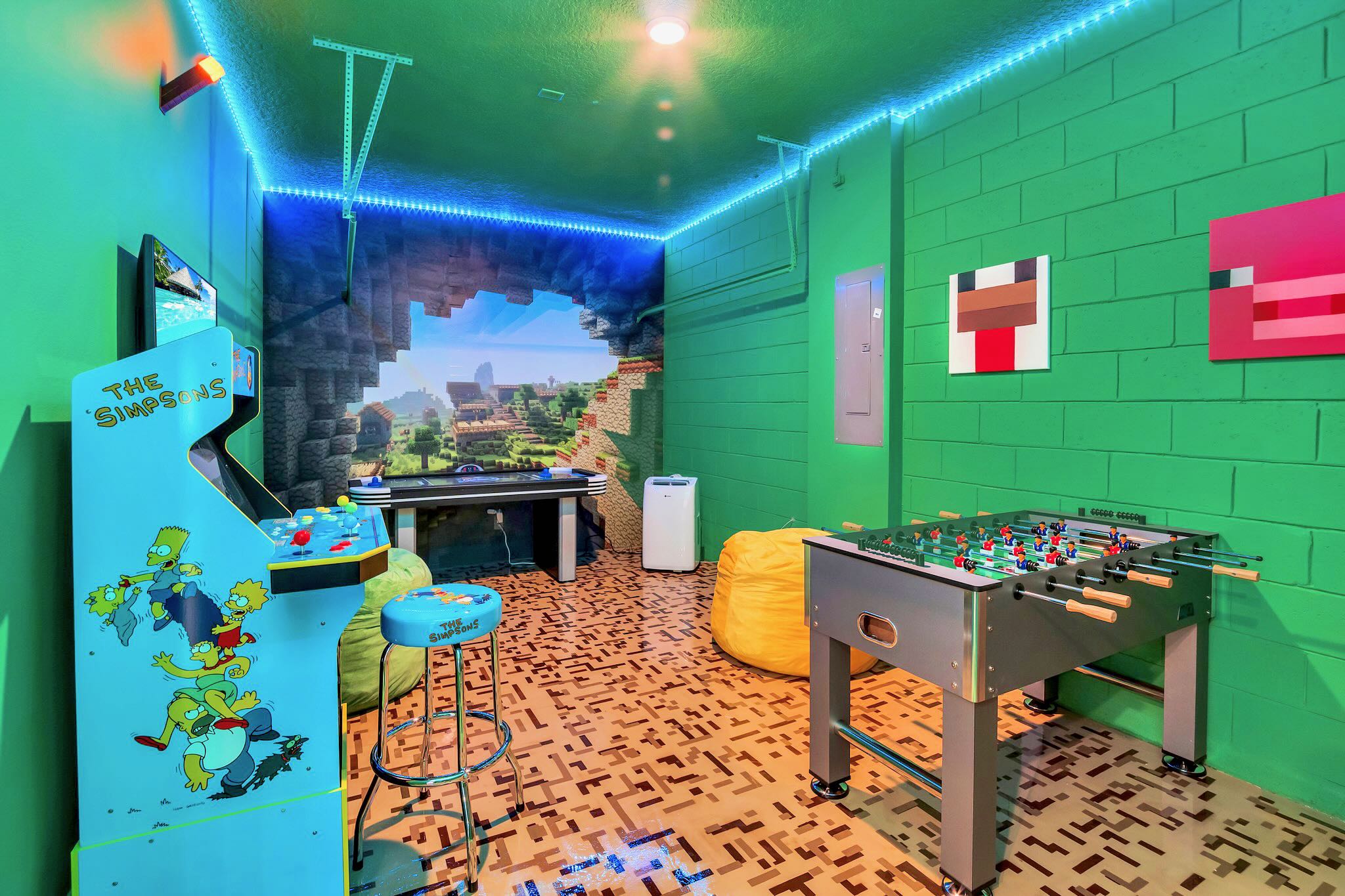 Vibrant game room with bright green textured walls, a foosball table, a Simpsons arcade machine, and a large Minecraft-themed wall mural, illuminated by blue LED strip lighting.