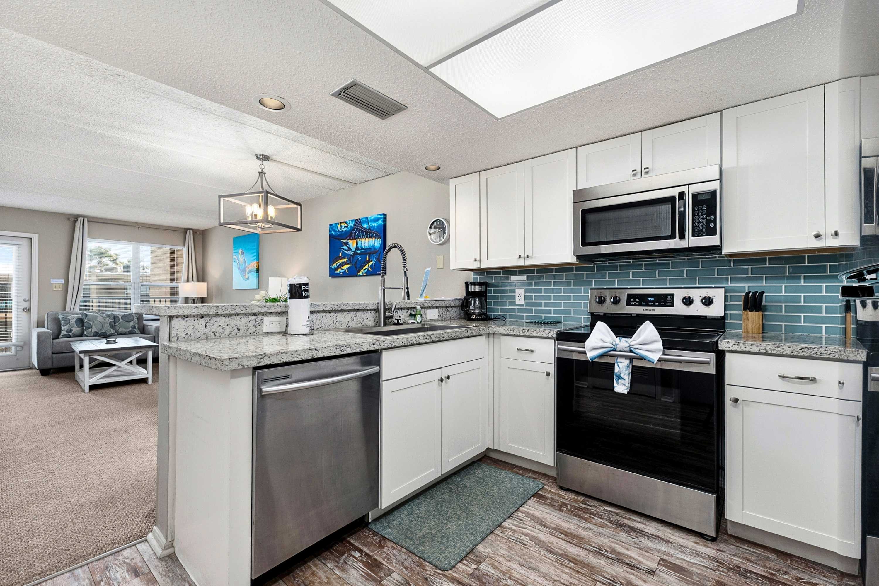 A well-equipped kitchen features white shaker cabinets, stainless steel appliances including a microwave, oven, and refrigerator, and a striking blue subway tile backsplash. Granite countertops and wood-look flooring complete the contemporary design.
