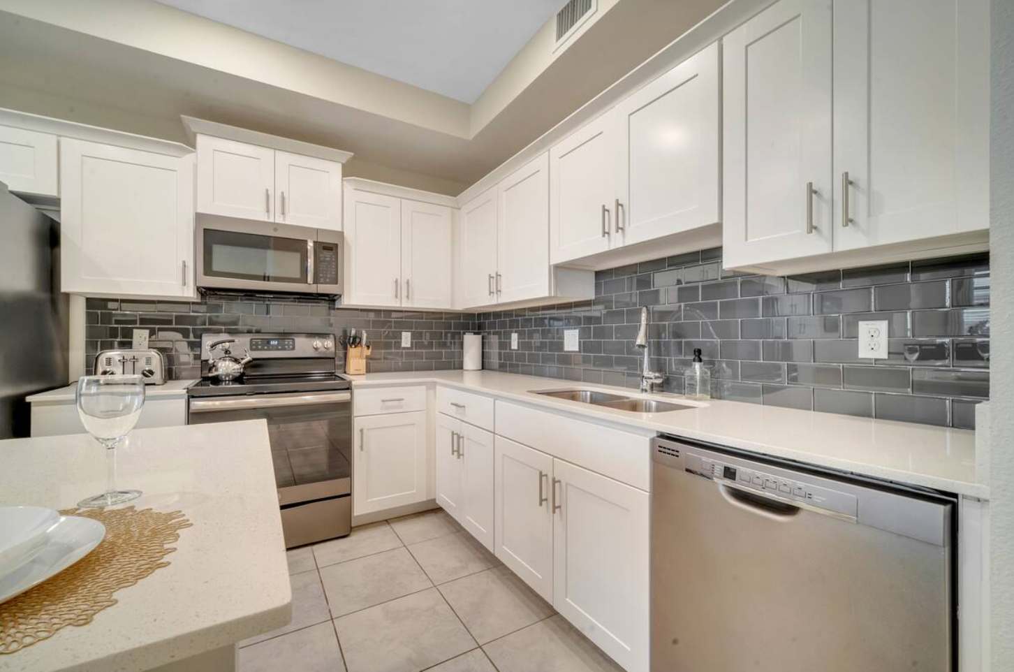 Modern kitchen with white shaker cabinets, light quartz countertops, and a dark gray subway tile backsplash. Stainless steel appliances include a microwave, range, and dishwasher.