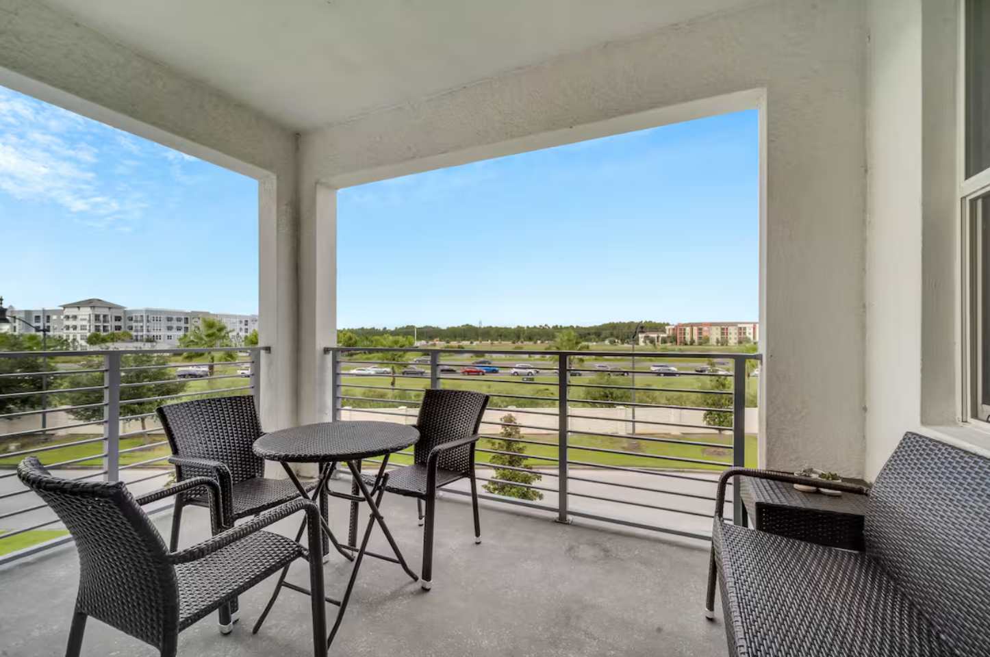 Spacious balcony with dark wicker outdoor furniture, offering an open view of the surrounding landscape and distant buildings under a clear blue sky.