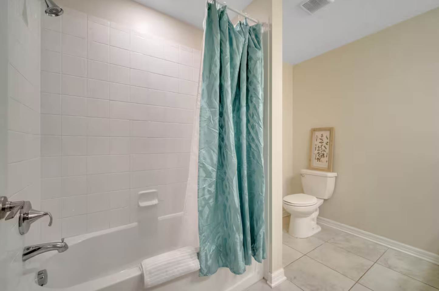 The shower and bathtub area of the second bathroom, featuring white tiled walls, a chrome shower head, and a vibrant teal shower curtain. A white towel is neatly folded on the tub edge.