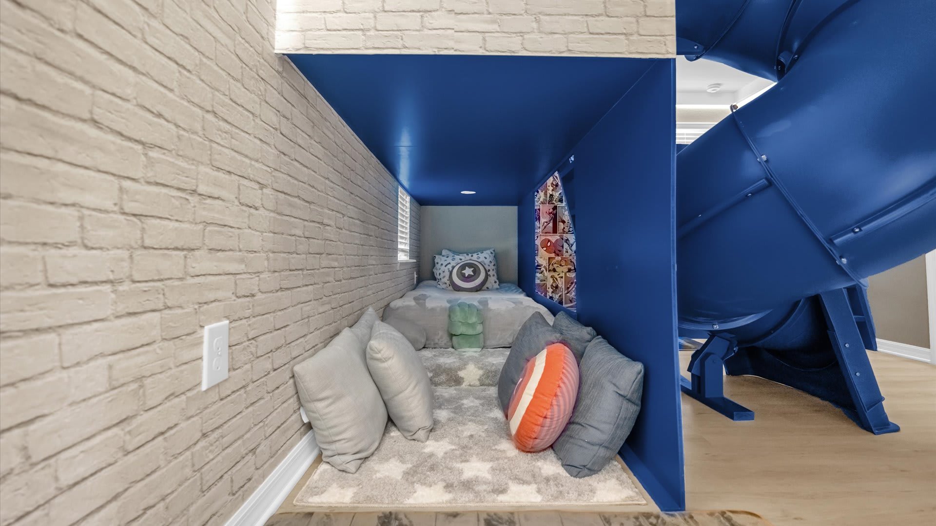 A unique, recessed sleeping nook within the kids' themed room, featuring a single bed, decorative pillows, and a soft rug. The light brick-patterned wall adds to the playful ambiance.