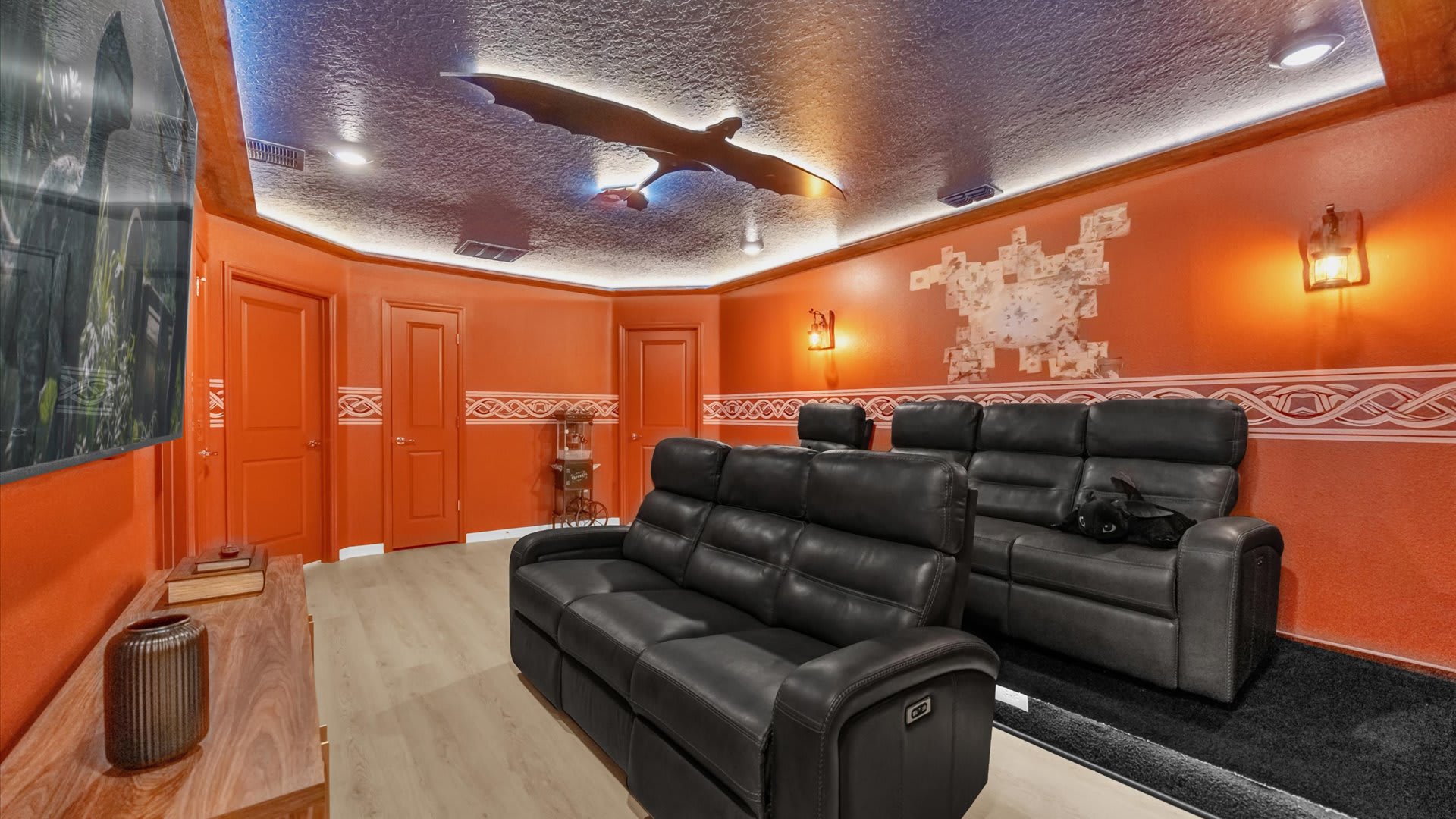 A vibrant orange-themed home cinema room features two rows of black reclining theater seats, a large projection screen, and a unique dragon sculpture on the ceiling, creating an immersive viewing experience.