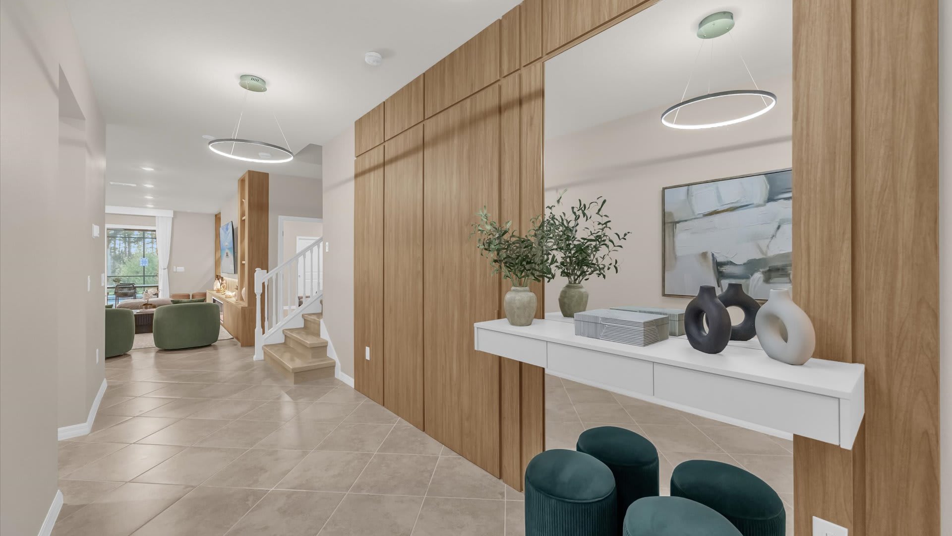 Modern entryway featuring a large mirror reflecting the opposite wall, a floating white console table with decorative items, and two teal velvet ottomans. A light wood paneled wall extends to the right, and a staircase is visible in the background.