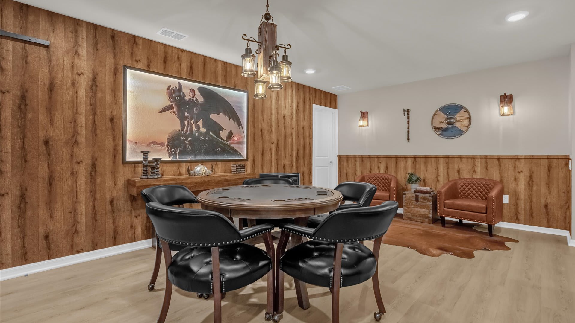 A themed game room features a round poker table with four black leather chairs, wood-paneled walls, and a large framed artwork of a dragon, creating a cozy and engaging atmosphere.