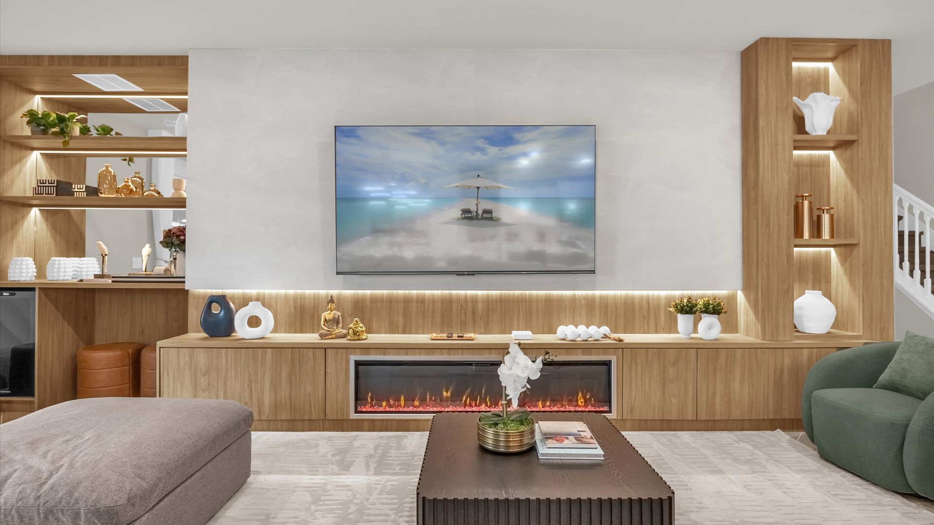 Contemporary living room with a large wall-mounted TV above a linear electric fireplace, set within a light wood media console. Integrated shelving units with accent lighting display decorative objects, and a dark coffee table sits on a light patterned rug.