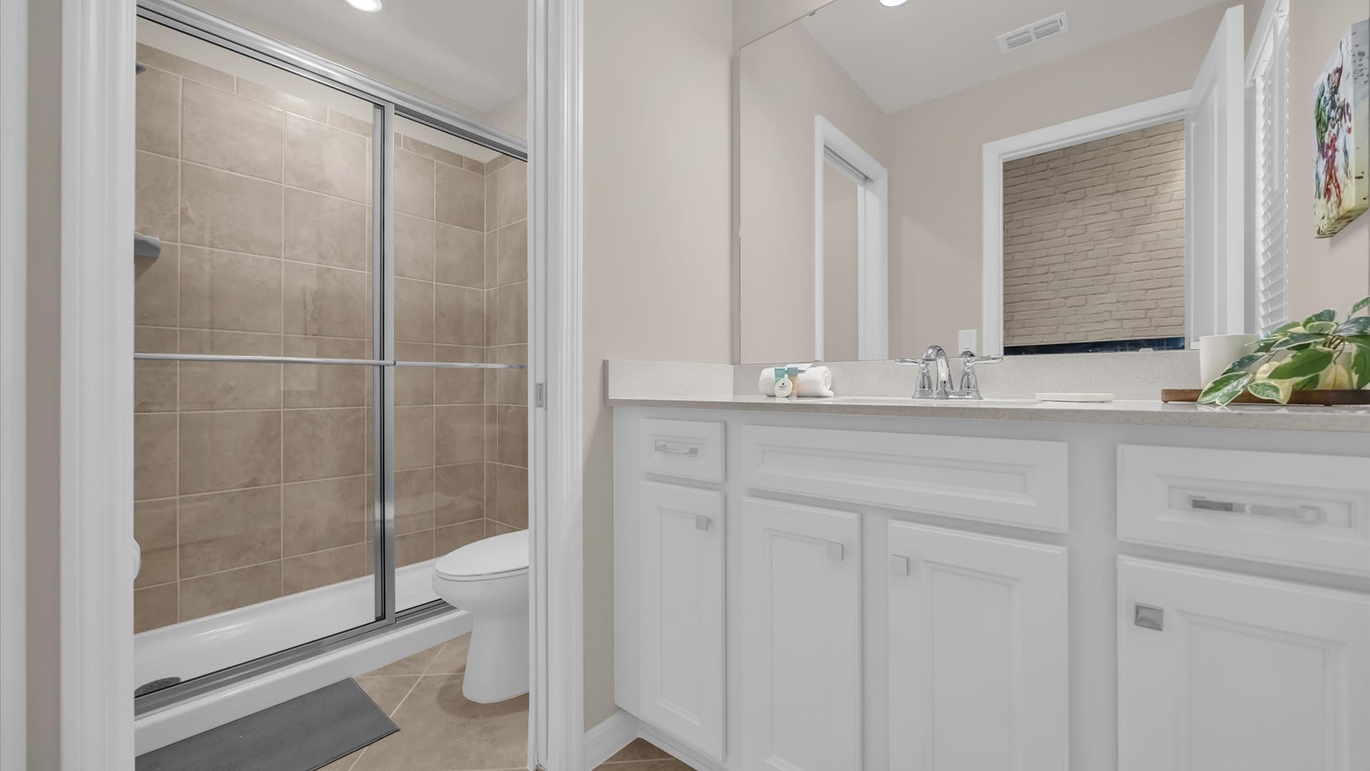A compact bathroom with a single white vanity, a light countertop, and a mirror. A glass-enclosed shower with beige tiled walls and a toilet inside is visible to the left.