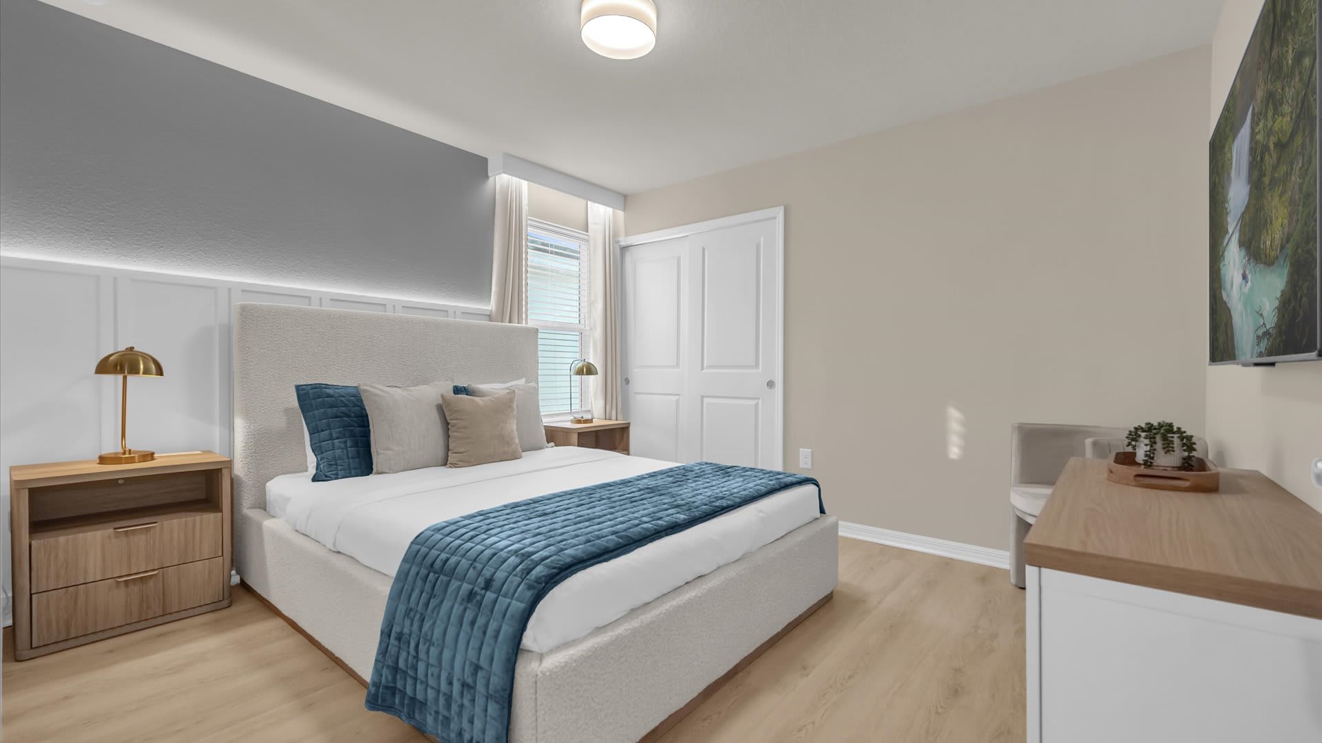 Cozy bedroom with a light-colored upholstered queen bed, blue and beige bedding, and a gray accent wall with wainscoting and integrated lighting. Two wooden nightstands with gold lamps flank the bed.