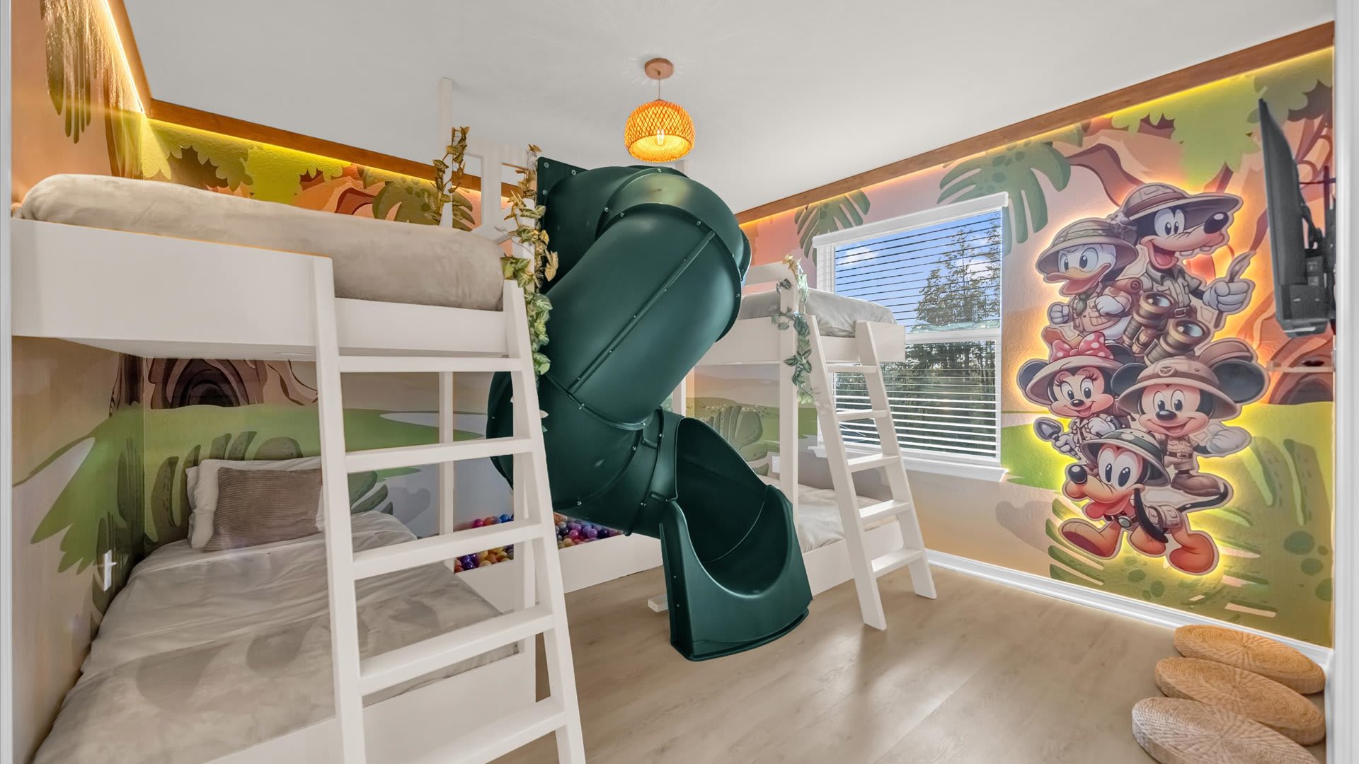 Themed kids' bedroom with white bunk beds, a dark green slide, and a colorful jungle mural featuring Mickey Mouse characters on the wall. Light wood flooring and a woven pendant light complete the playful space.