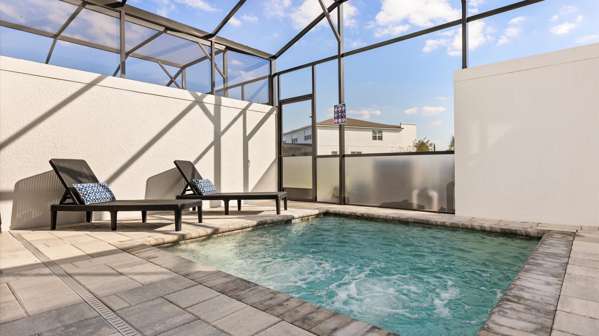 Close-up view of the private hot tub with bubbling water, flanked by two dark lounge chairs with patterned blue pillows, within a screened enclosure.